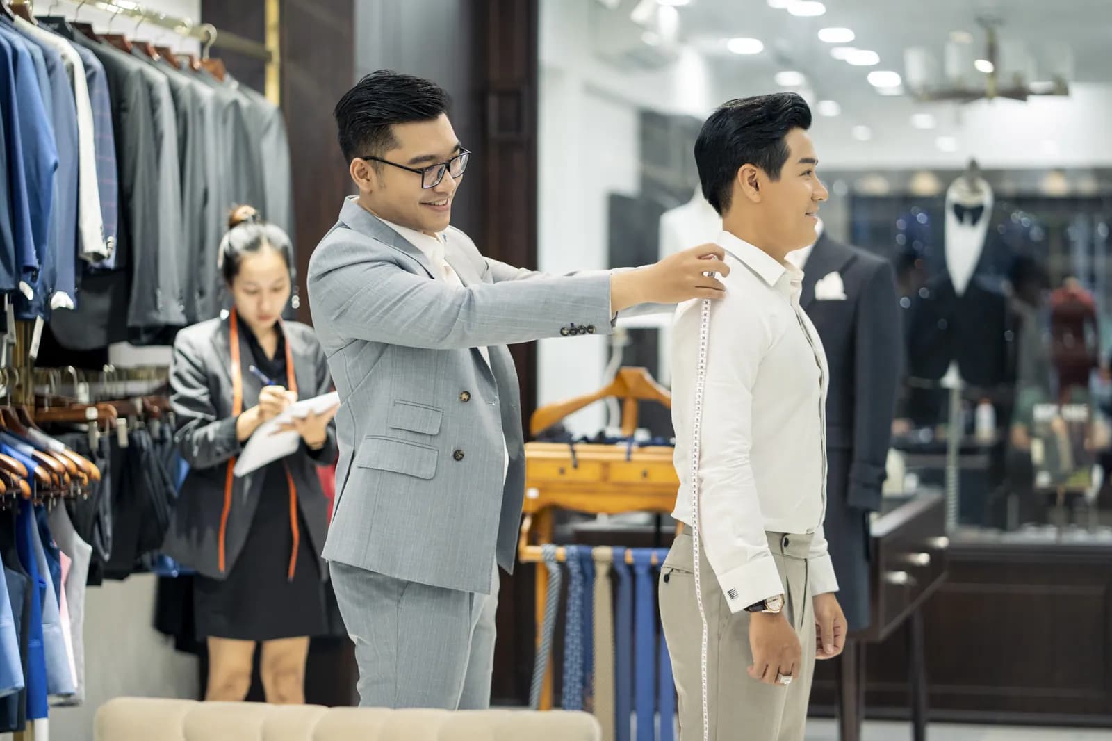 Lấy số đo vai trên sơ mi, trợ lý ghi số đo bên cạnh