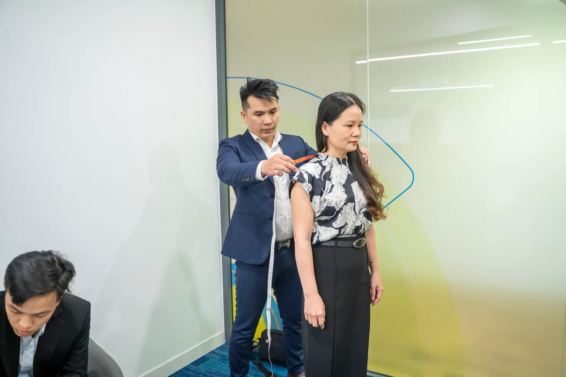 Đo vai cho chị nhân viên, sau lưng là vách kính văn phòng ACBS