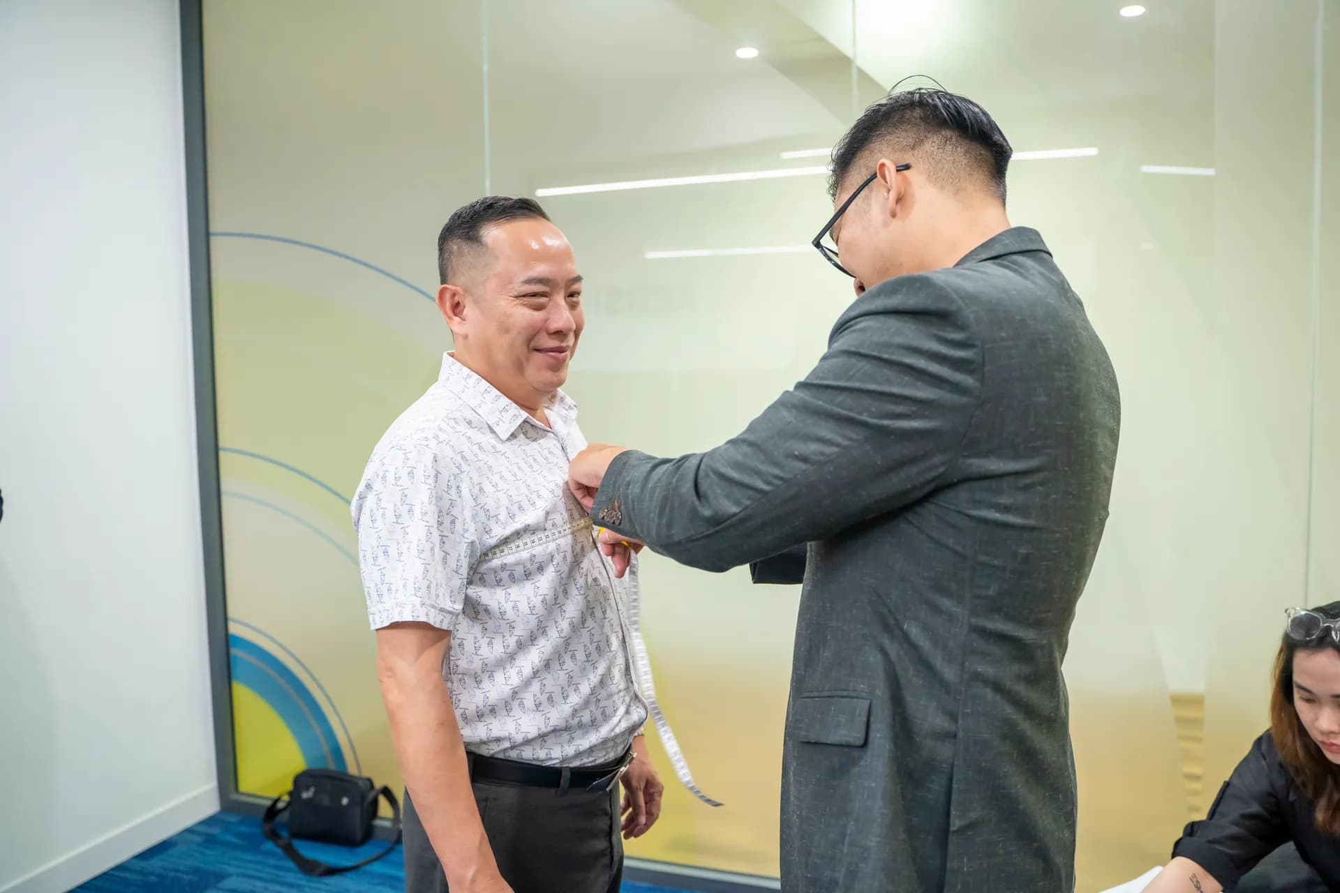 Thợ may vest xám đo vai cho khách áo sơ mi kẻ sọc, khách mỉm cười