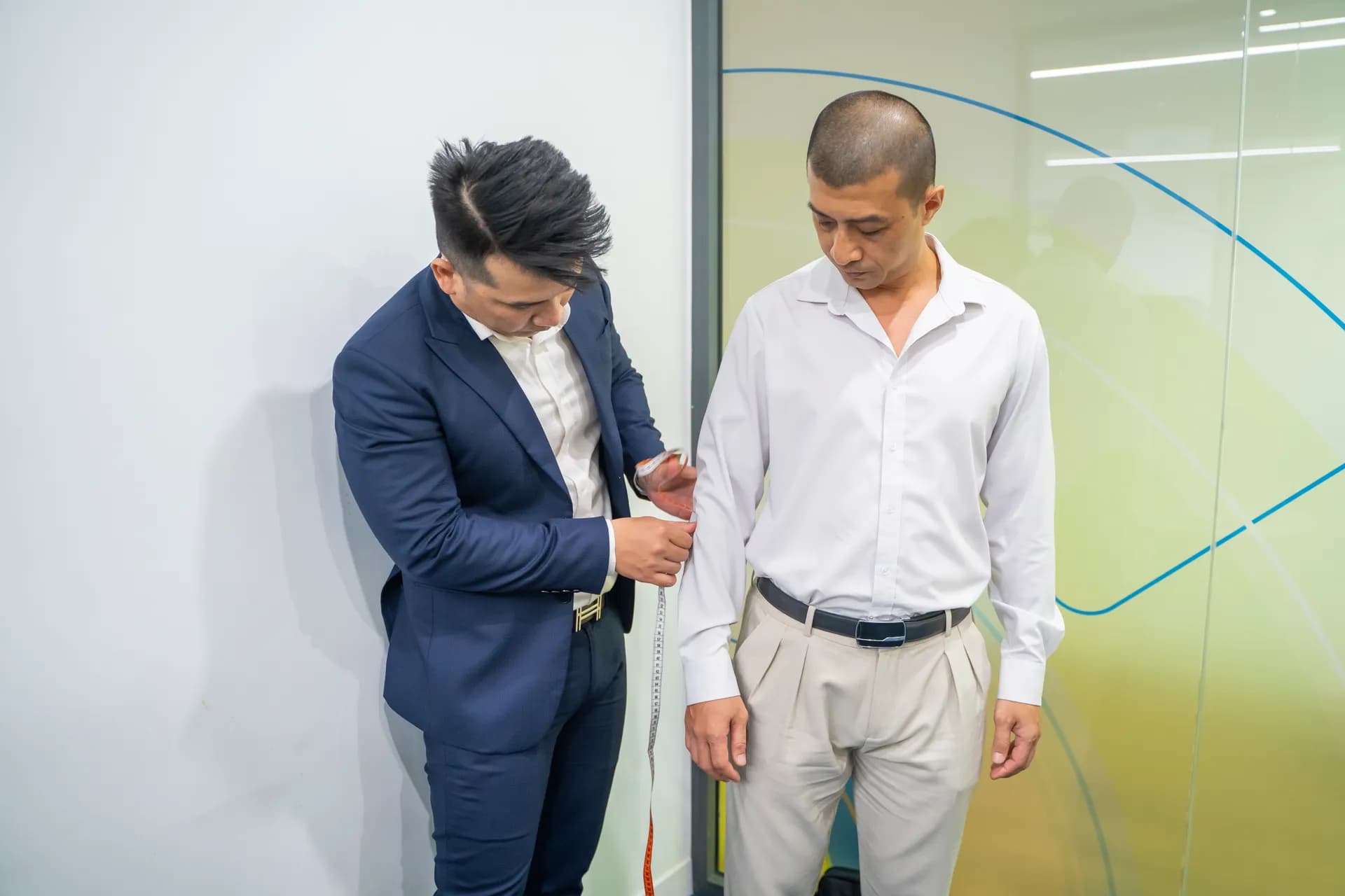 Thợ may vest navy đo ngang ngực khách áo sơ mi trắng, quần be