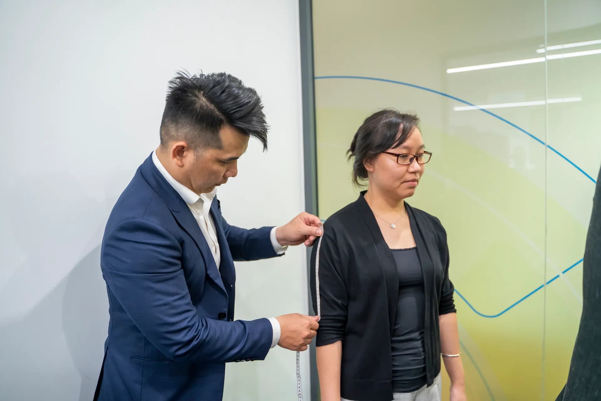 Thợ may vest navy cẩn thận đo chiều dài tay cho khách nữ áo khoác đen