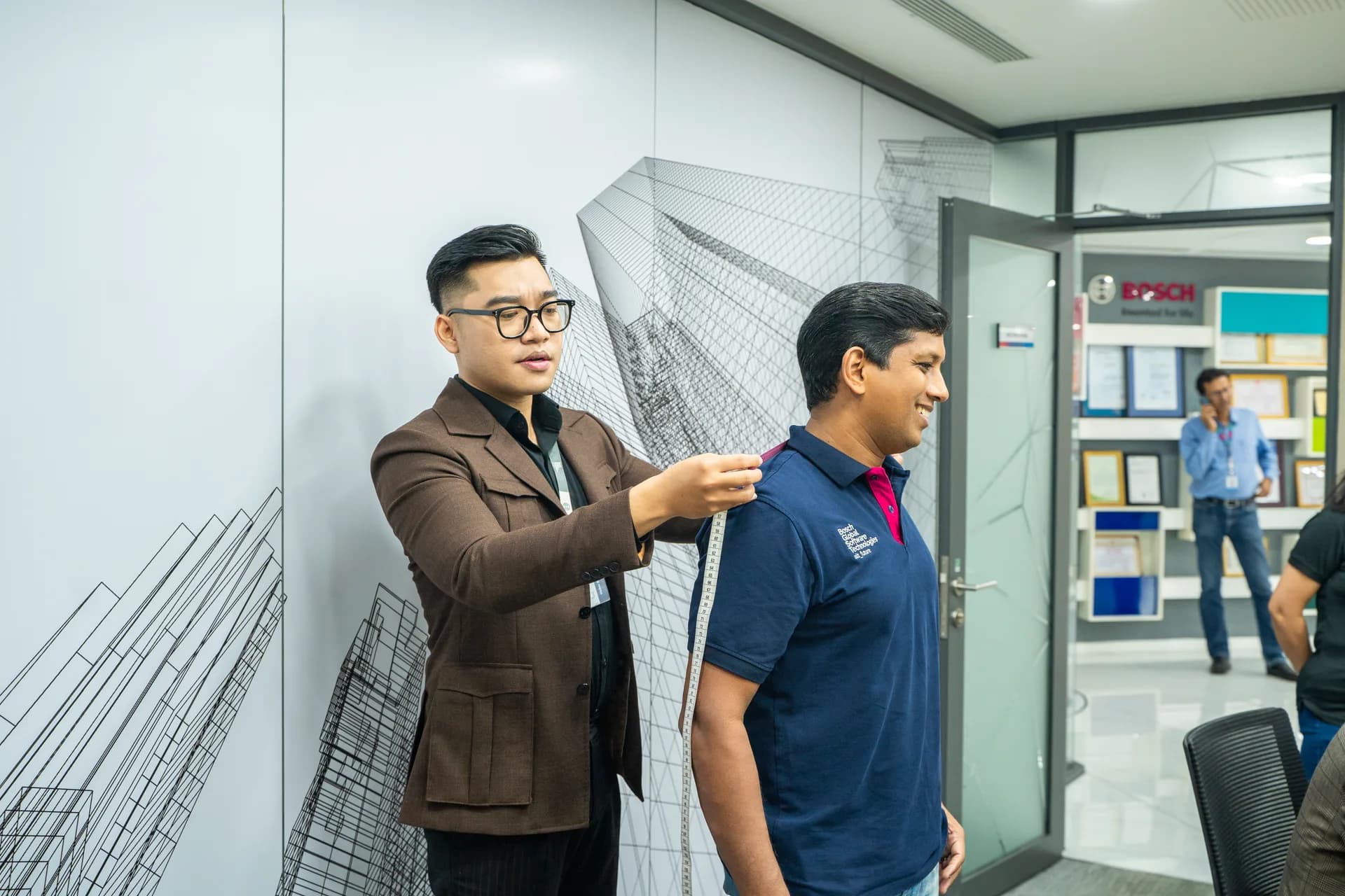 Đo vai cho nhân viên nam áo polo, cửa kính văn phòng BOSCH phía sau