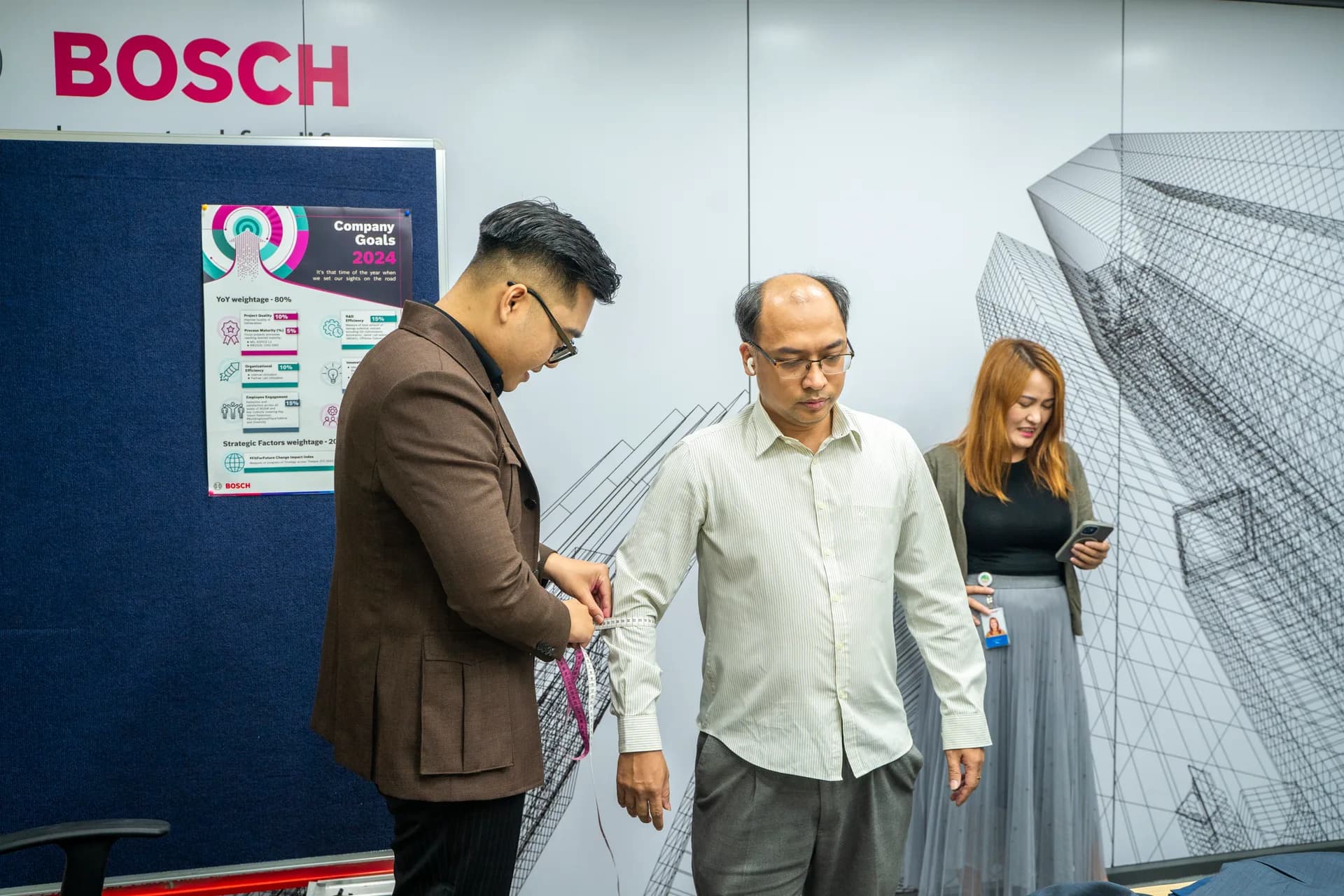 Đo eo cho nhân viên áo sơ mi, sau lưng là bảng logo BOSCH