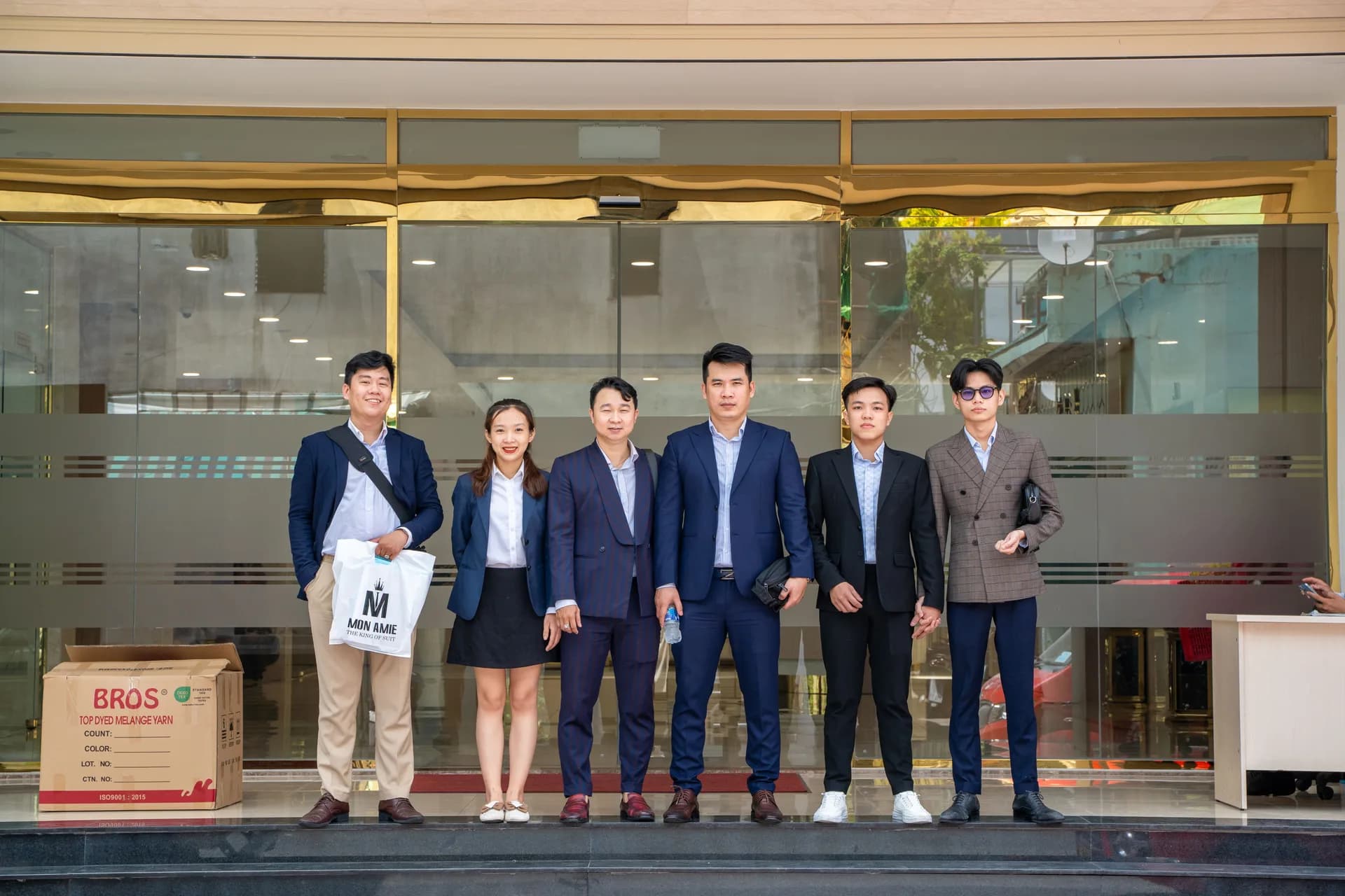 Nhóm nhân viên Mon Amie giao đồng phục, chụp ảnh trước cửa kính công ty