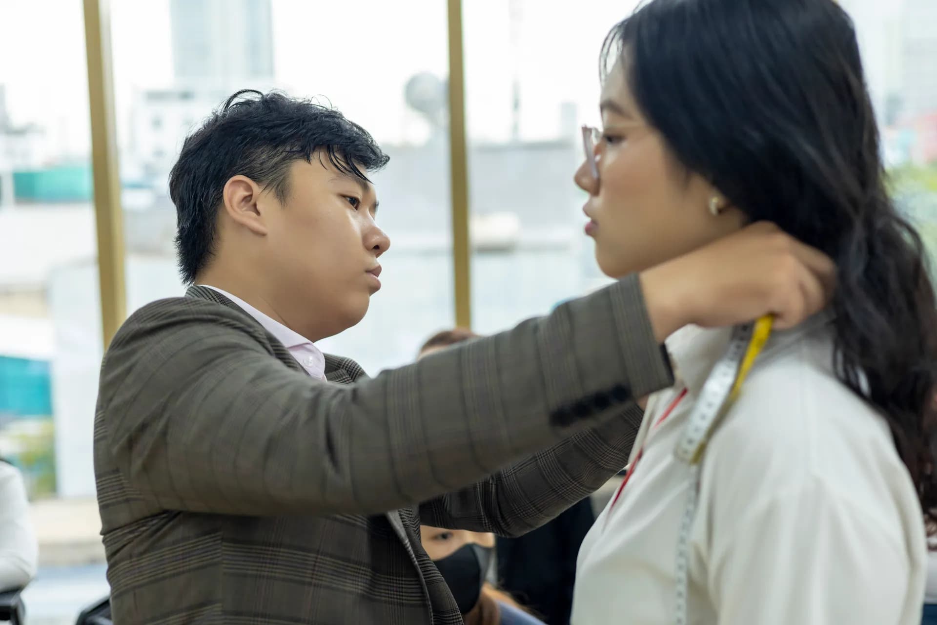 Thợ may vest kẻ đo vòng cổ cho khách nữ áo sơ mi trắng bên cửa sổ sáng