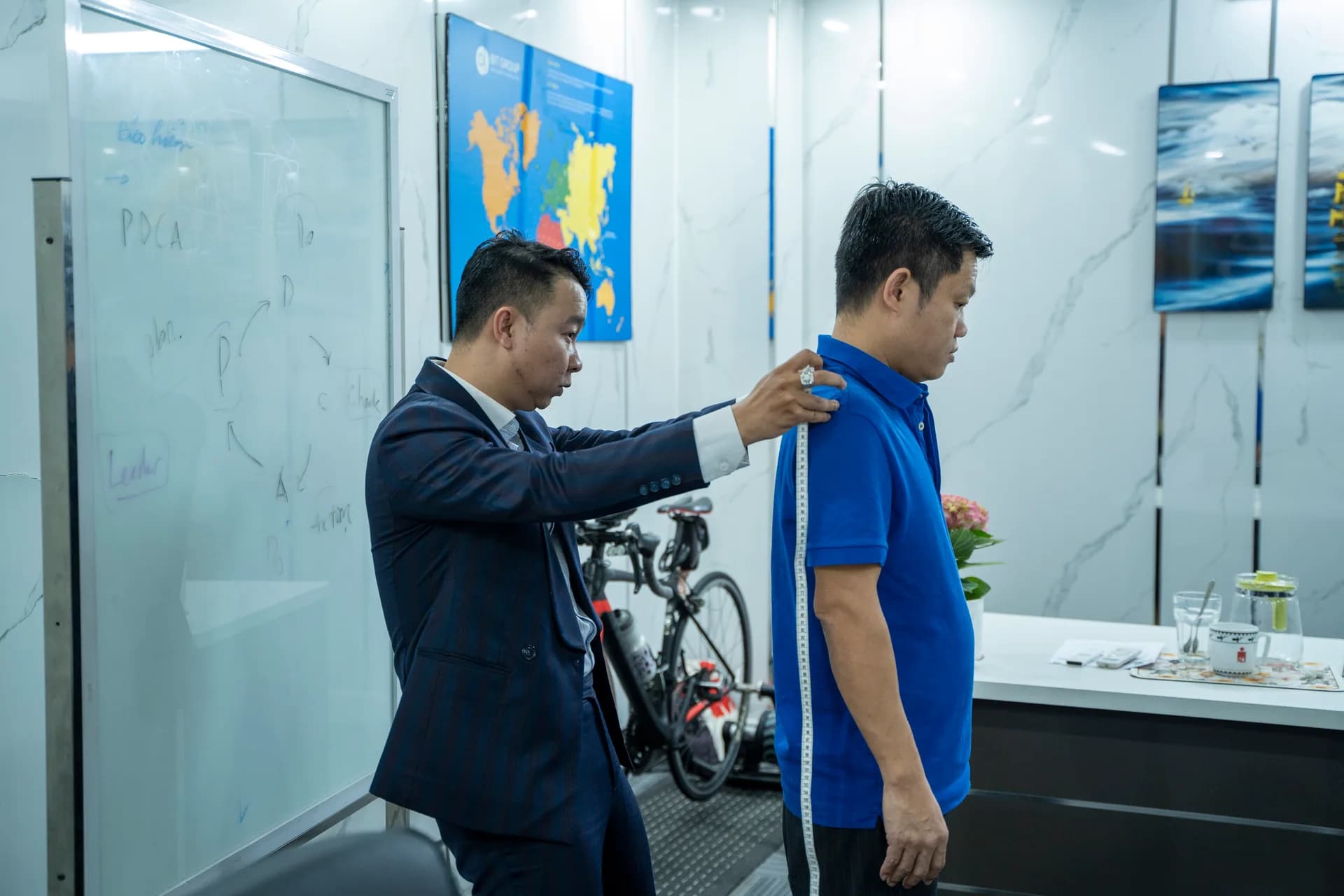 Đo chiều dài lưng cho nhân viên nam áo polo xanh ngay phòng làm việc