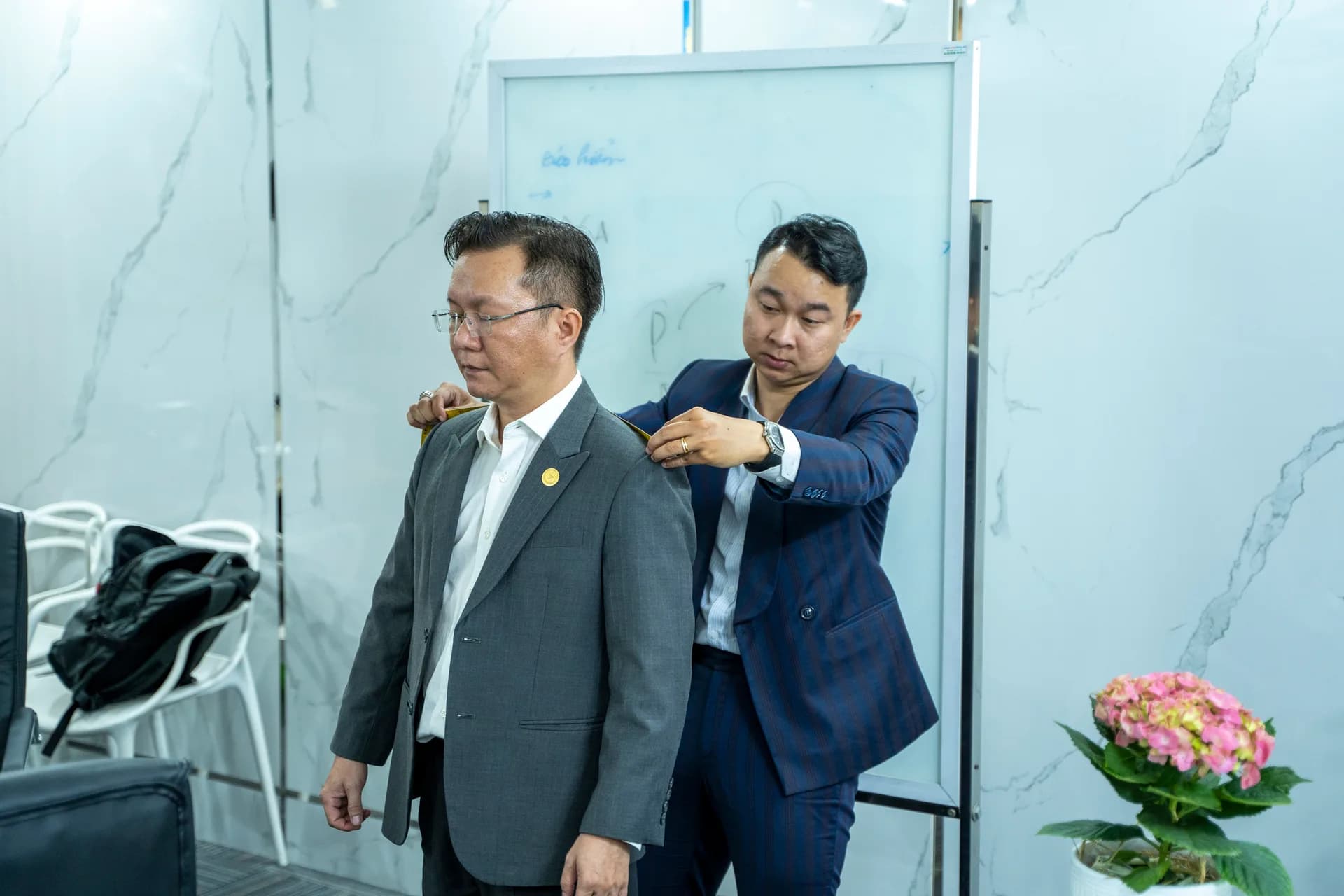 Đo vai cho anh lãnh đạo áo vest xám trong văn phòng công ty