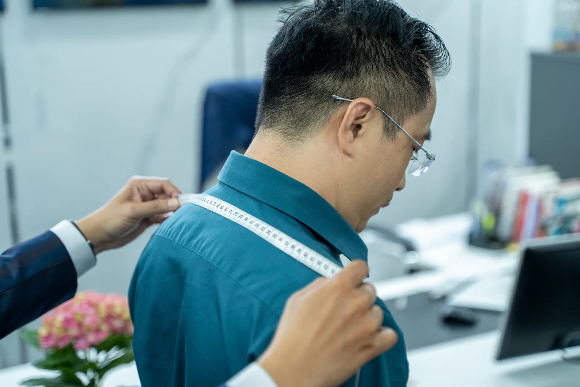 Cận cảnh thước dây vắt ngang vai áo sơ mi xanh cổ vịt, nền văn phòng mờ