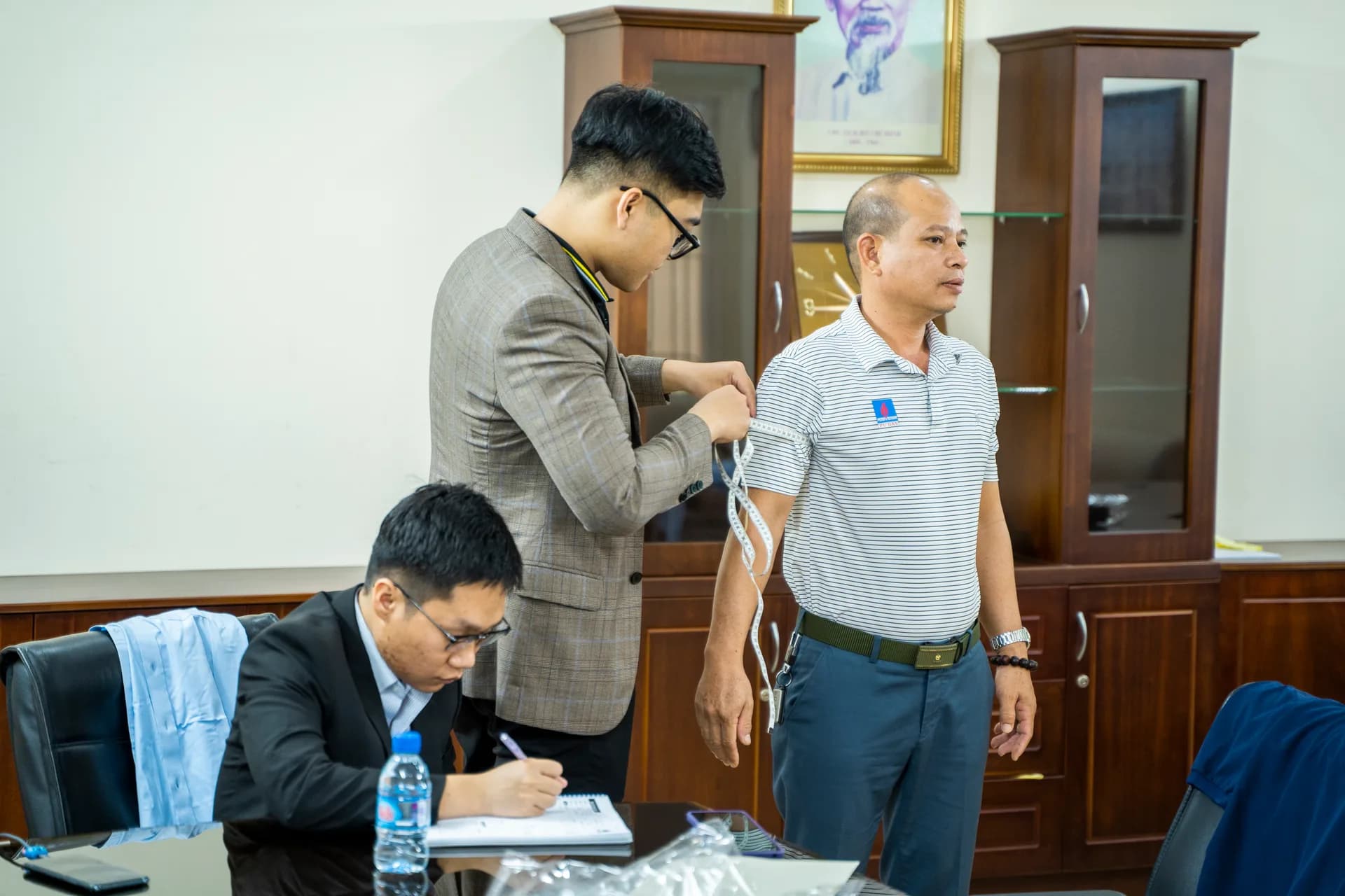 Đo bắp tay cán bộ mặc áo polo PV GAS, nhân viên ghi số đo bên cạnh