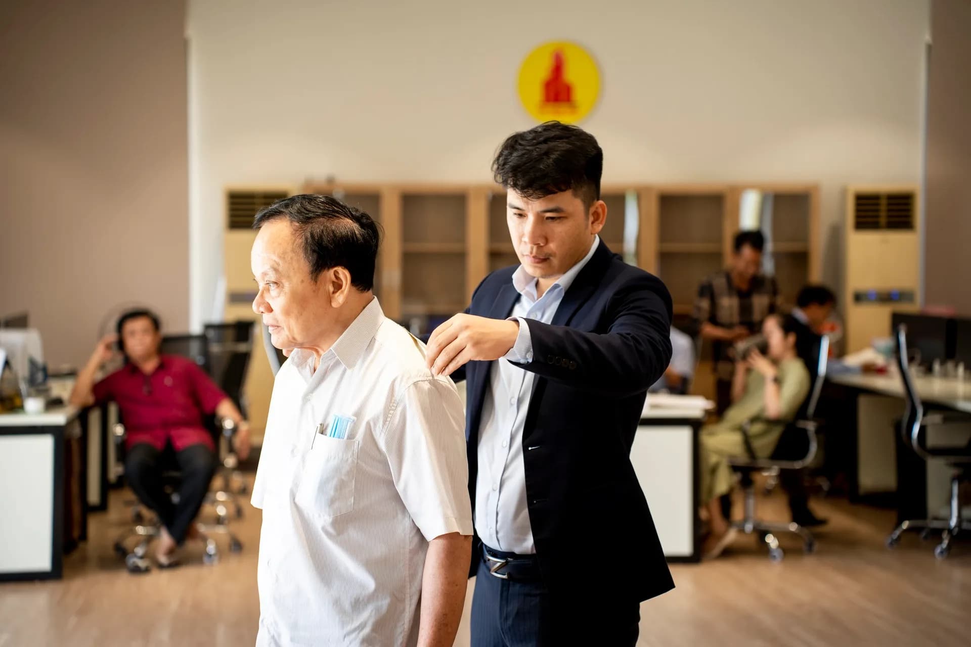 Đo vai cho cán bộ lớn tuổi, đồng nghiệp ngồi phía sau