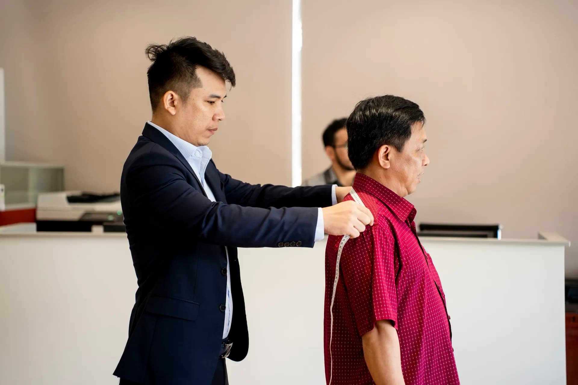 Thợ may vest navy đo chiều dài tay áo cho khách nam áo sơ mi đỏ đô, nền sáng