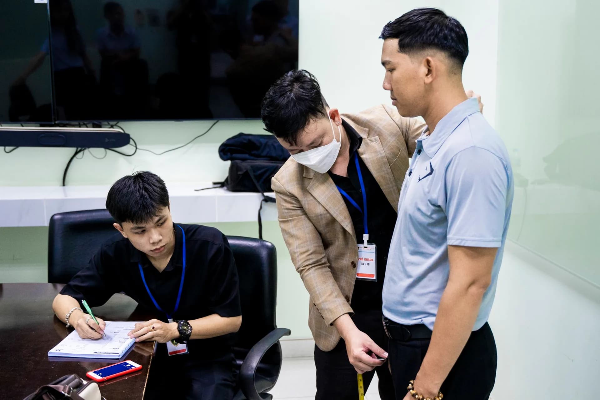 Đo dài quần cho nhân viên, người ghi số đo ngồi bên bàn họp