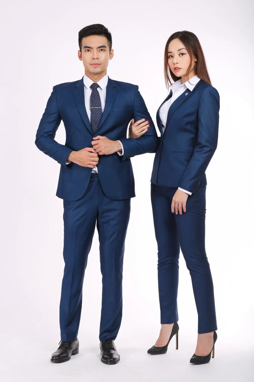 Cặp đồng phục xanh navy, nam chỉnh áo, nữ khoác tay, nền studio sáng