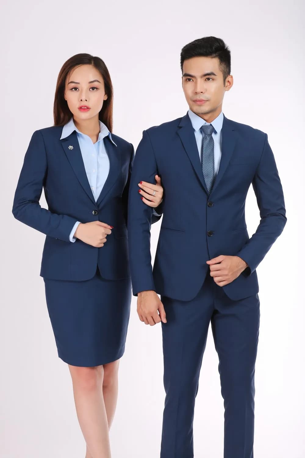 Cặp đồng phục xanh navy, nam nữ khoác tay, ánh nhìn tự tin trên nền sáng