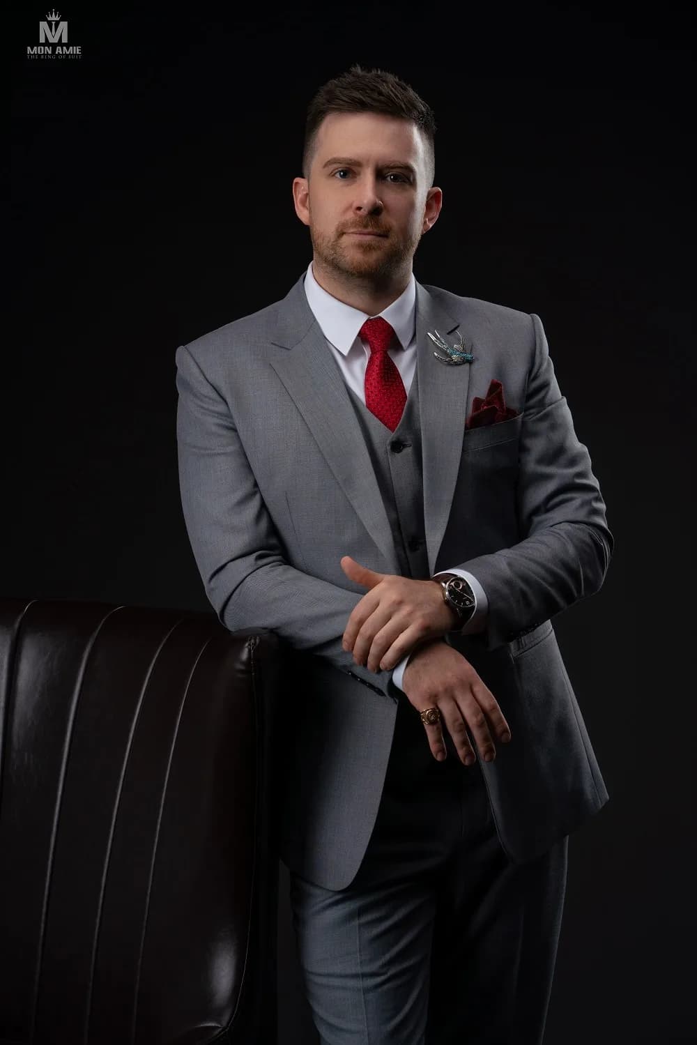 Suit xám ba mảnh, cà vạt đỏ và ghim cài áo tinh xảo, minh họa nút cà vạt Windsor cân đối