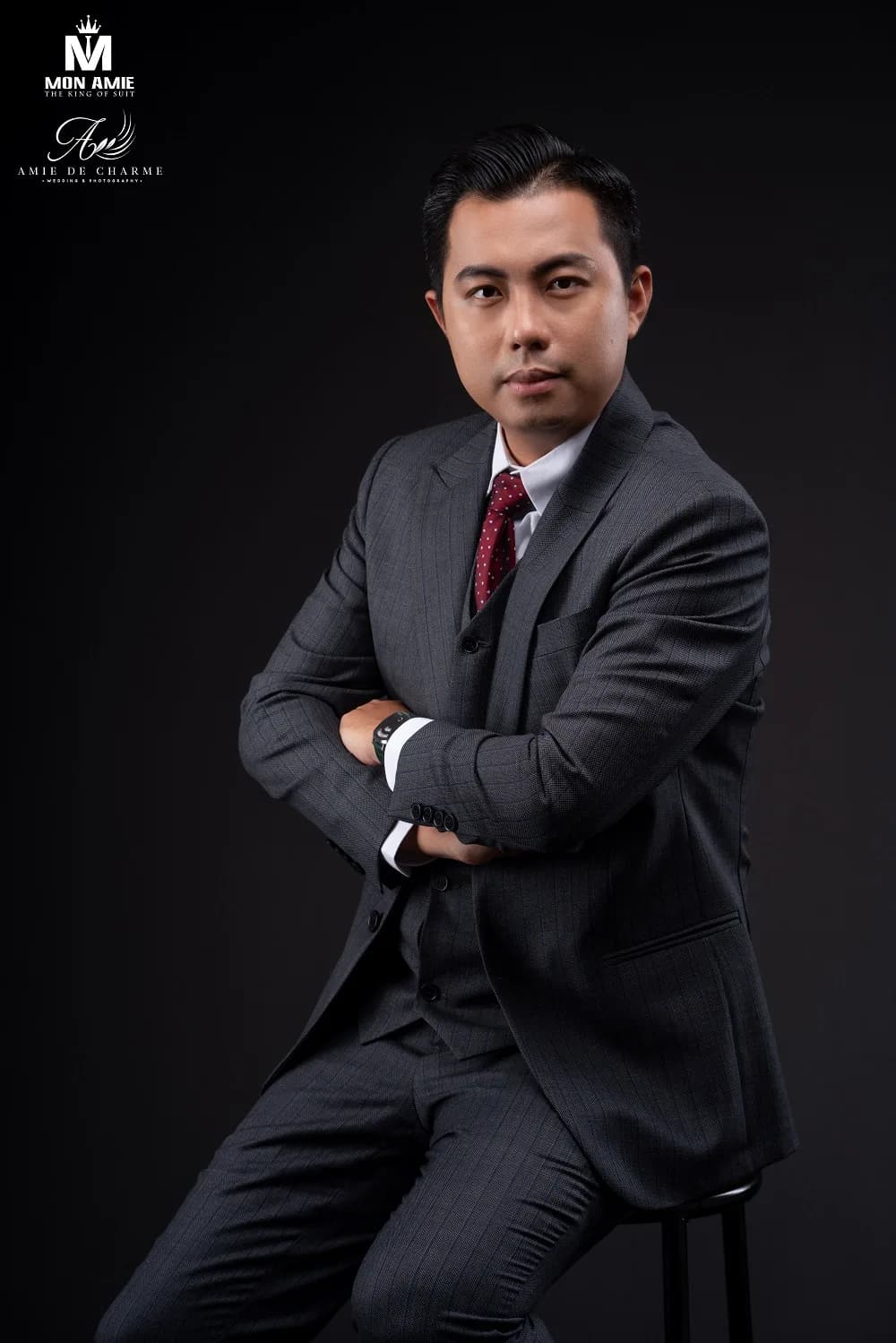 Chân dung doanh nhân trong suit ba mảnh xám kẻ sọc, cà vạt đỏ đô, ngồi ghế cao khoanh tay, hình ảnh may đo vest cao cấp