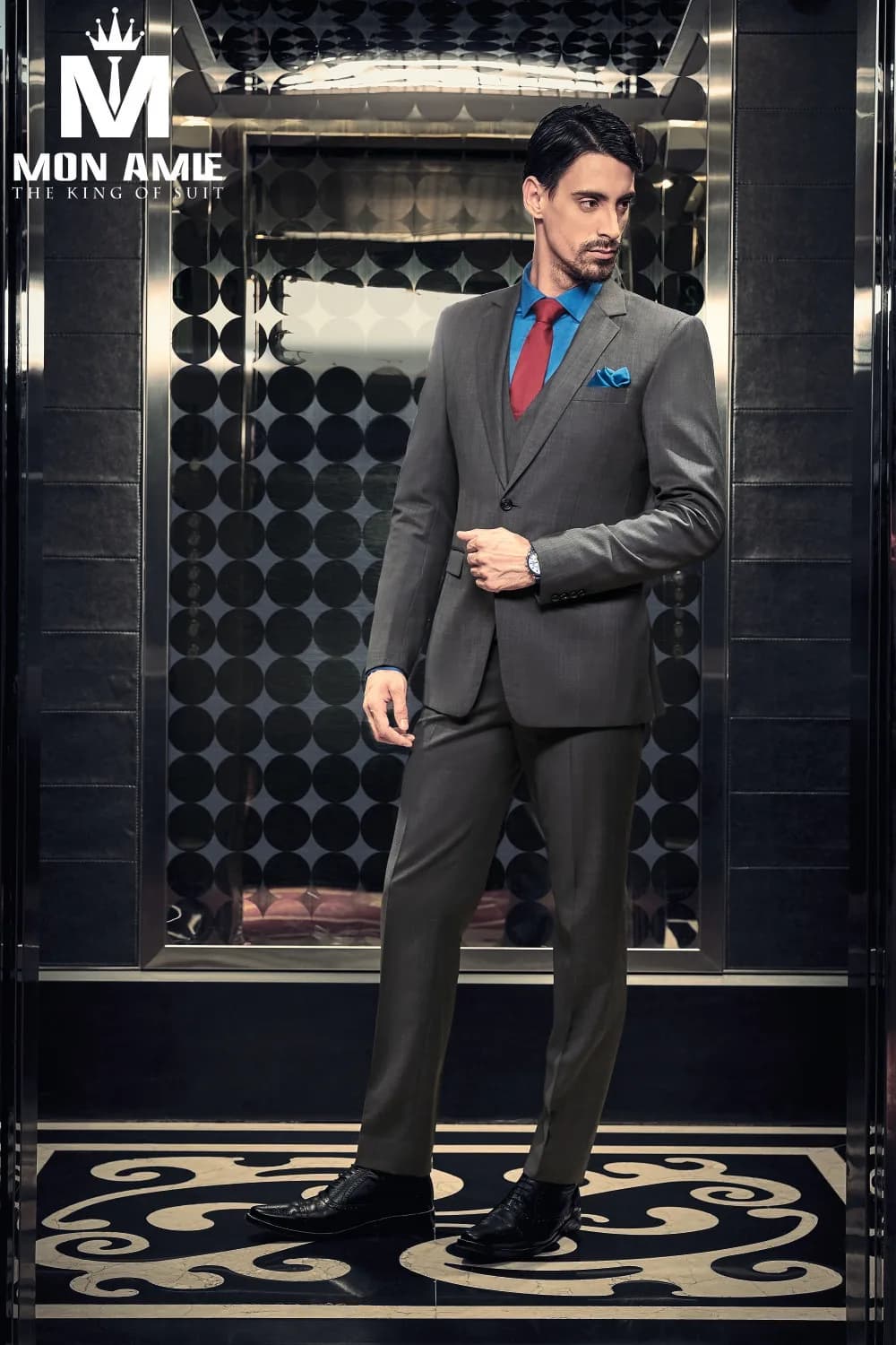 Suit xám ba mảnh, sơ mi xanh dương và cà vạt đỏ đô trong thang máy đen bóng, phong cách vest trung niên nam