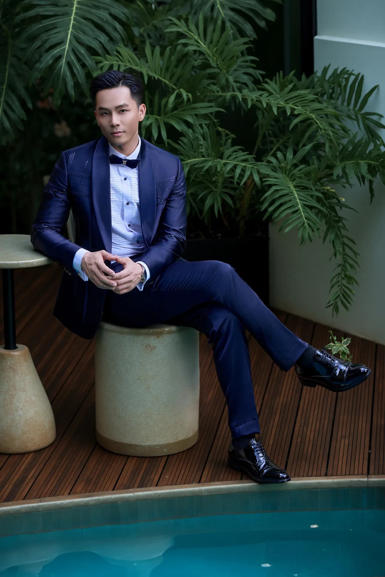 Chi tiết lưng áo suit đen kim tuyến đỏ rượu chạy ngang, nền tường viền vàng.