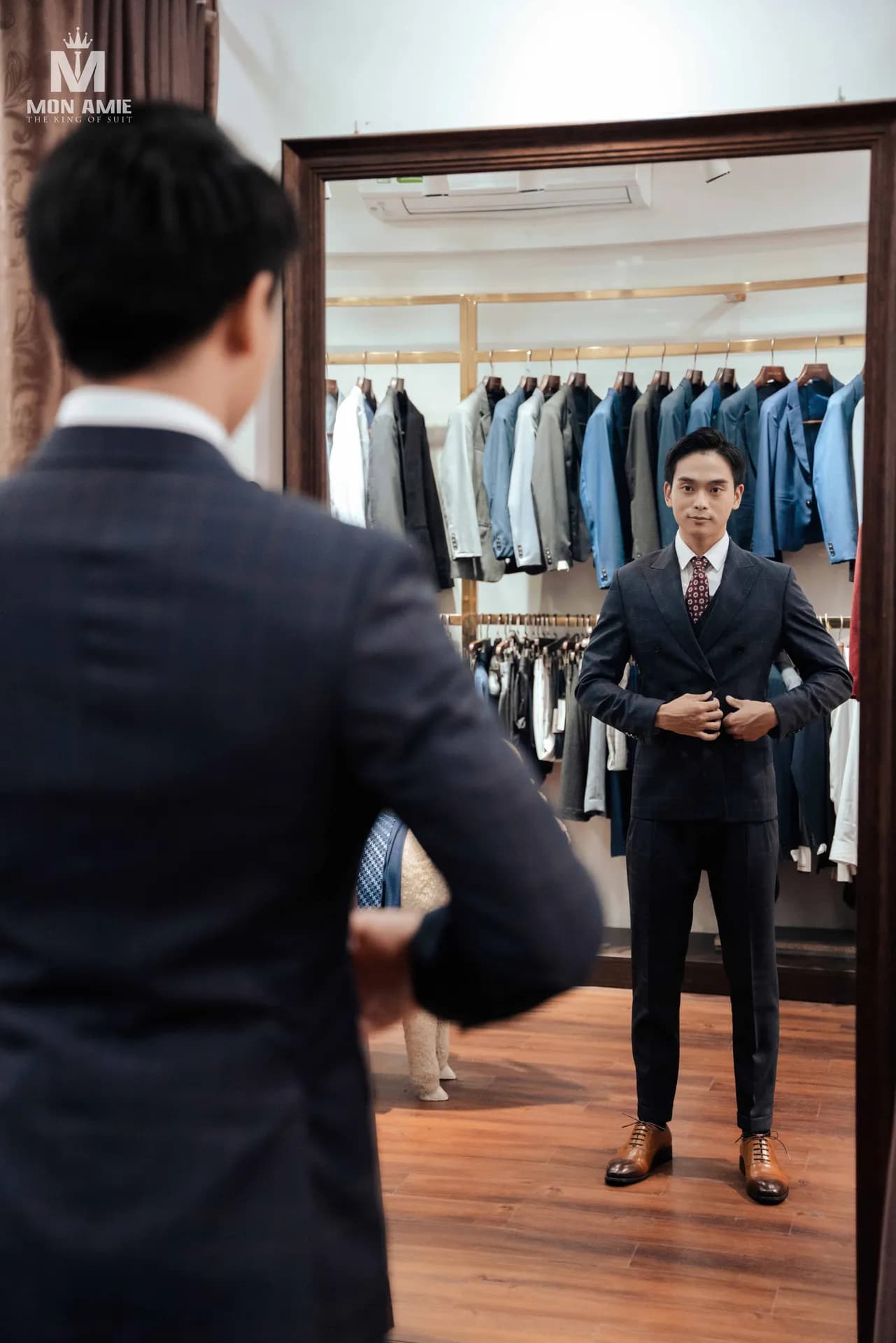 Khách soi gương cài khuy vest hai hàng caro đậm, giá vest treo phía sau