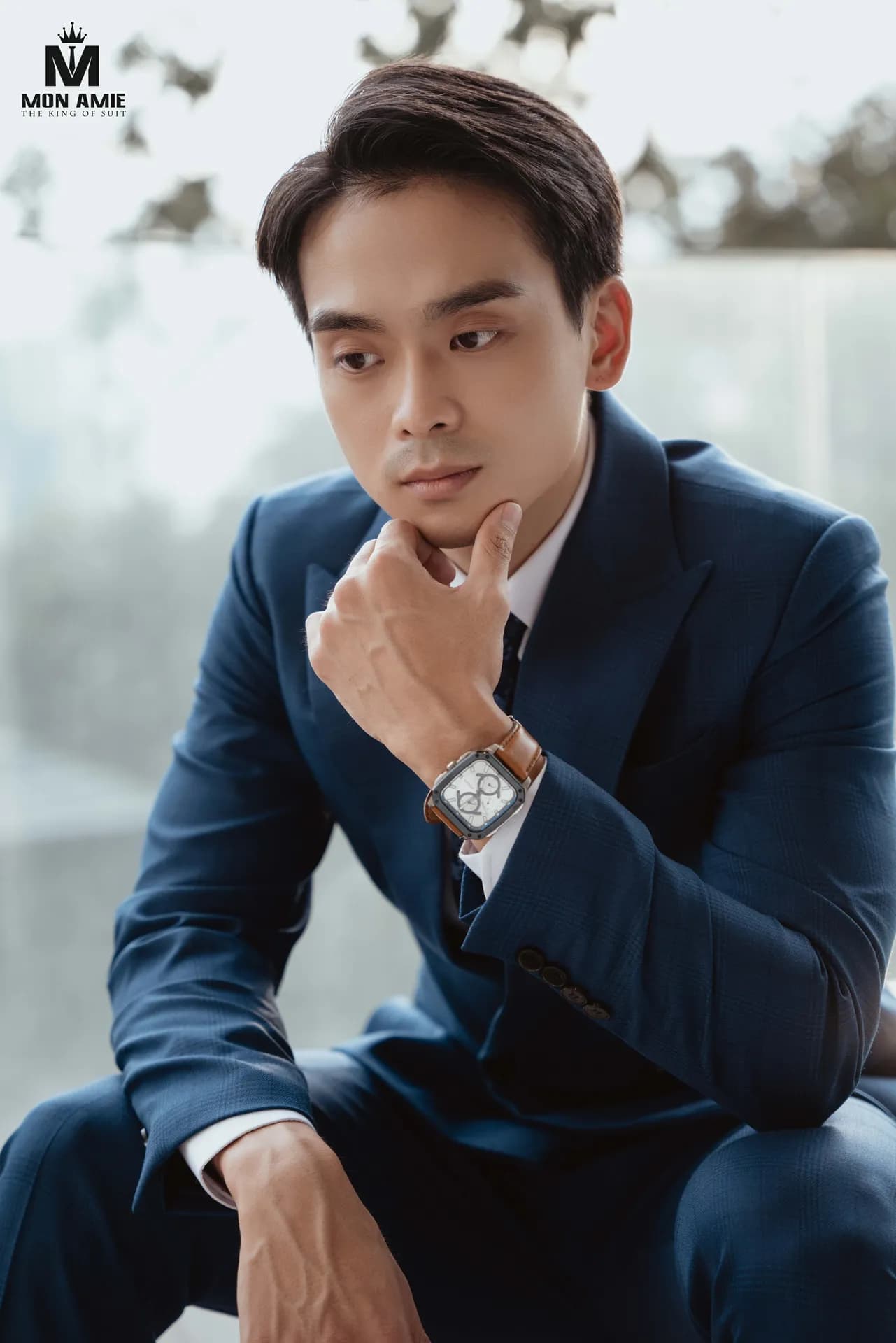 Cận cảnh suit xanh navy hai hàng khuy, tay chống cằm, đồng hồ da nâu