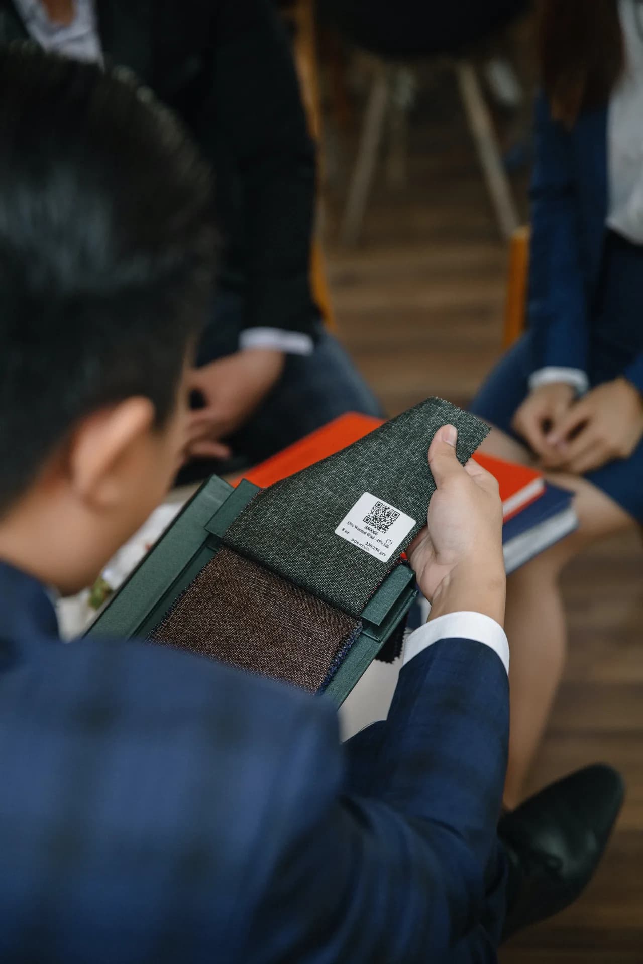 Cận cảnh bàn tay chạm mẫu vải len lụa Dormeuil trong sổ mẫu, minh họa vì sao giá vải may vest chênh lệch