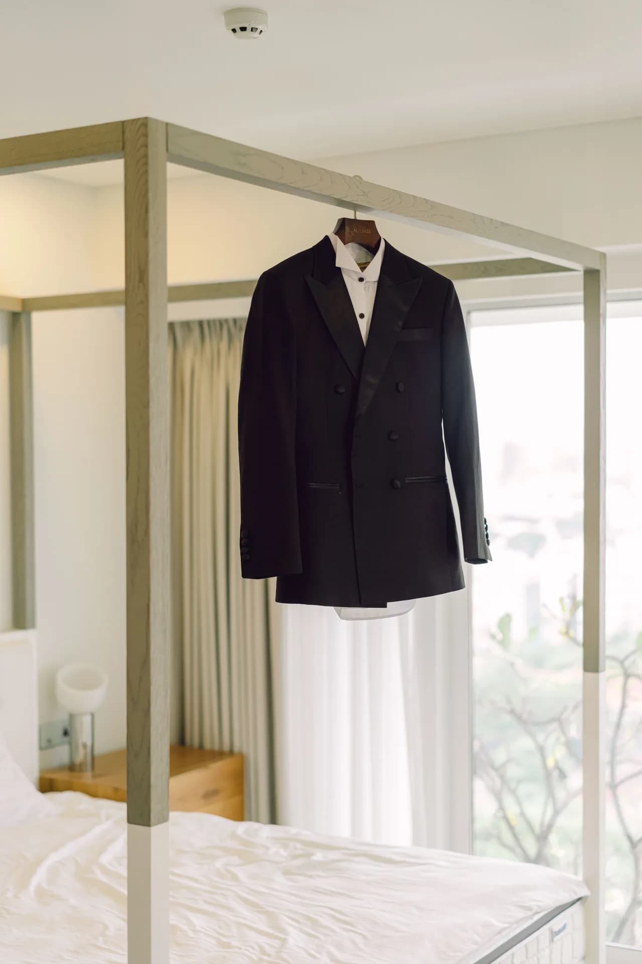 Tuxedo cài hai hàng khuy treo trên khung giường, ánh sáng cửa sổ dịu