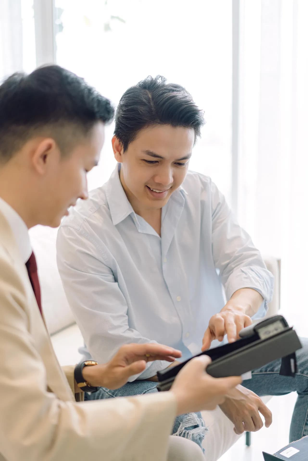 Khách mỉm cười chọn mẫu vải cùng thợ may trong ánh sáng cửa sổ