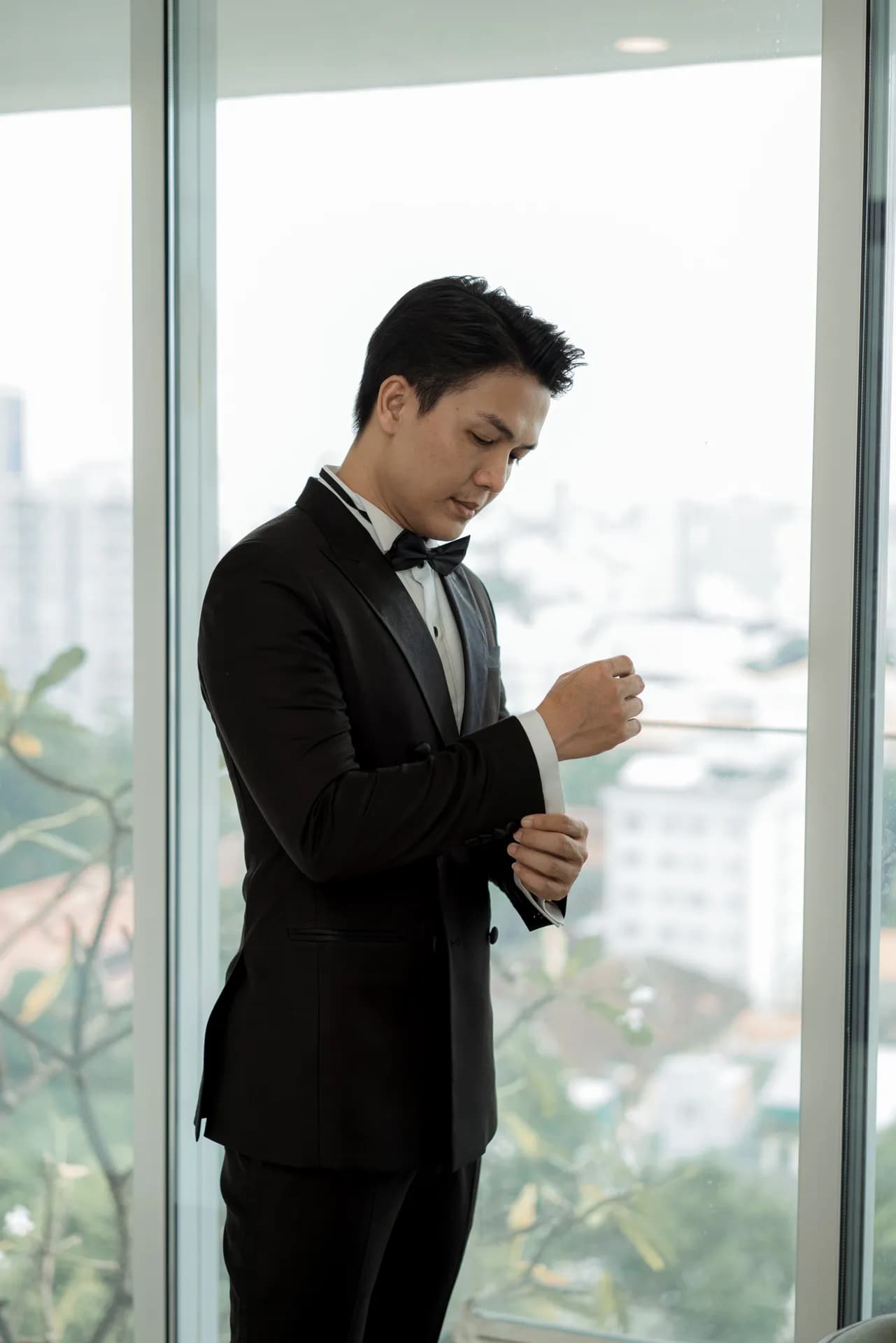 Tuxedo đen nơ đen, chỉnh khuy măng sét bên cửa kính