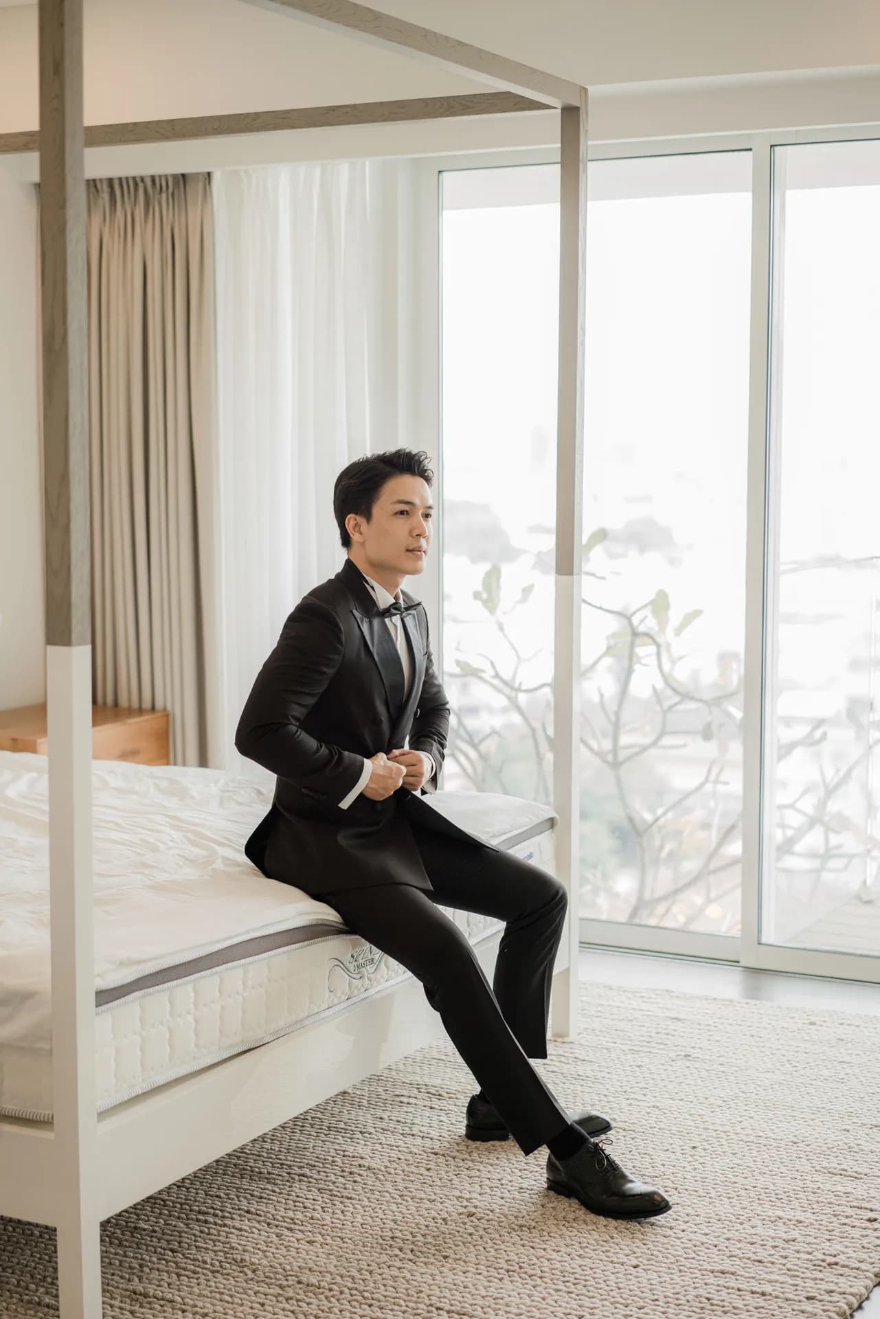 Tuxedo đen cổ lụa, ngồi mép giường cài khuy áo