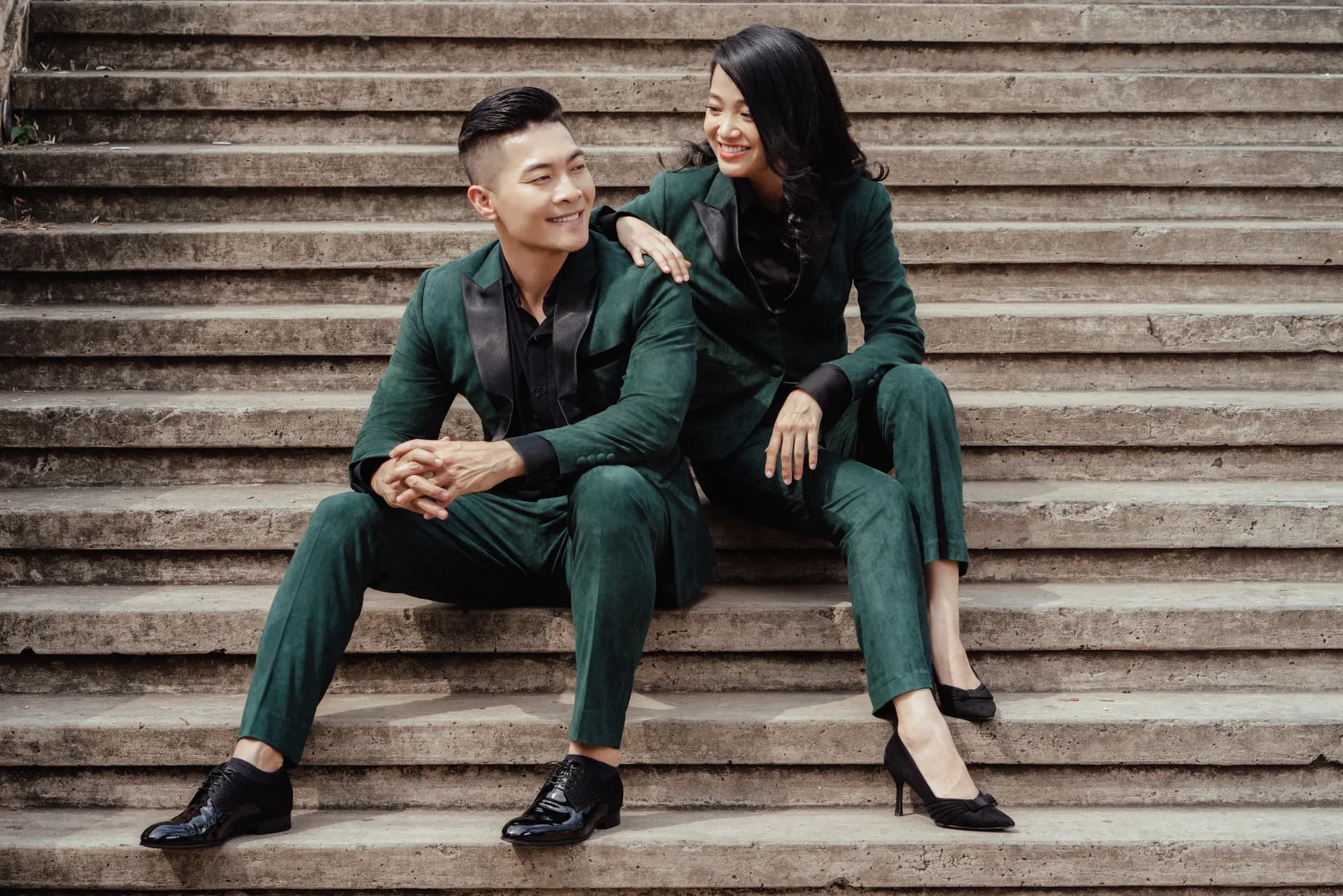 Cặp đôi suit nhung xanh lục cổ lụa đen, ngồi cười trên bậc thang