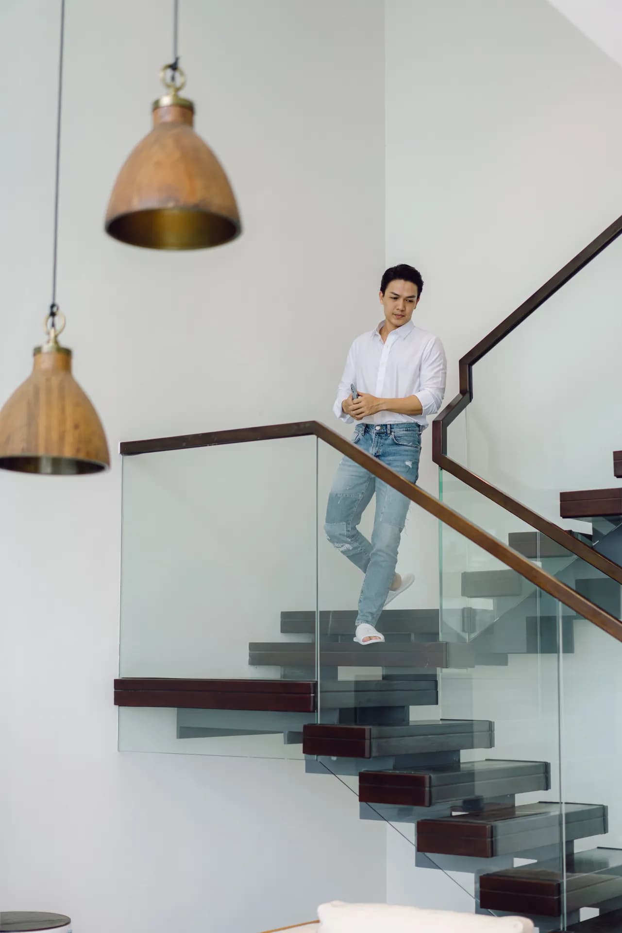 Khách sơ mi trắng bước xuống cầu thang kính, đèn thả gỗ