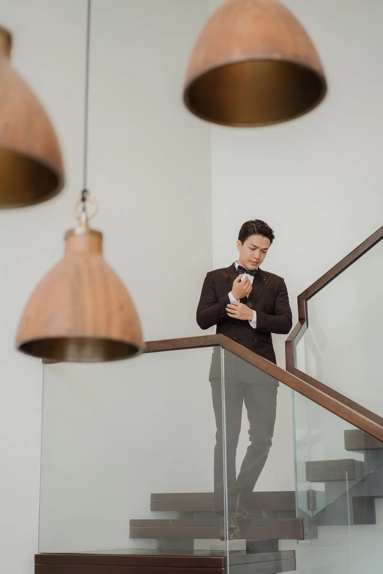 Tuxedo đen chỉnh măng sét bên cầu thang kính và đèn thả