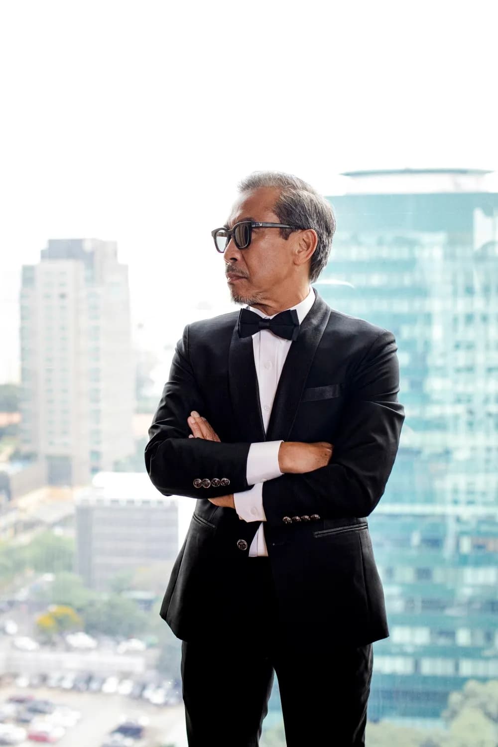 Tuxedo nhung đen thắt nơ, khoanh tay, nền cửa sổ nhìn ra thành phố
