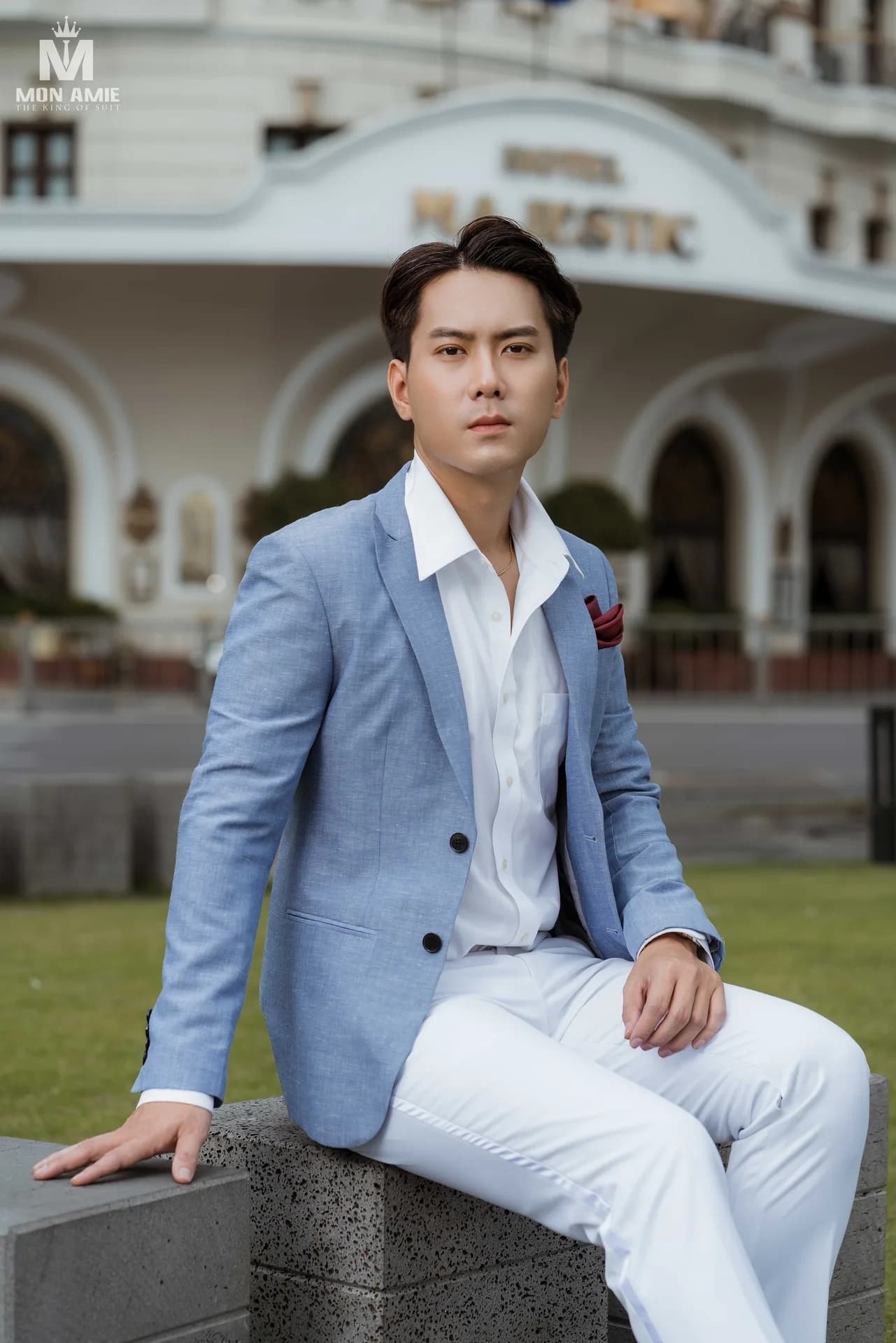 Blazer xanh lanh phối quần trắng, ngồi trên bệ đá trước tòa nhà cổ, minh họa mặc vest khác màu quần