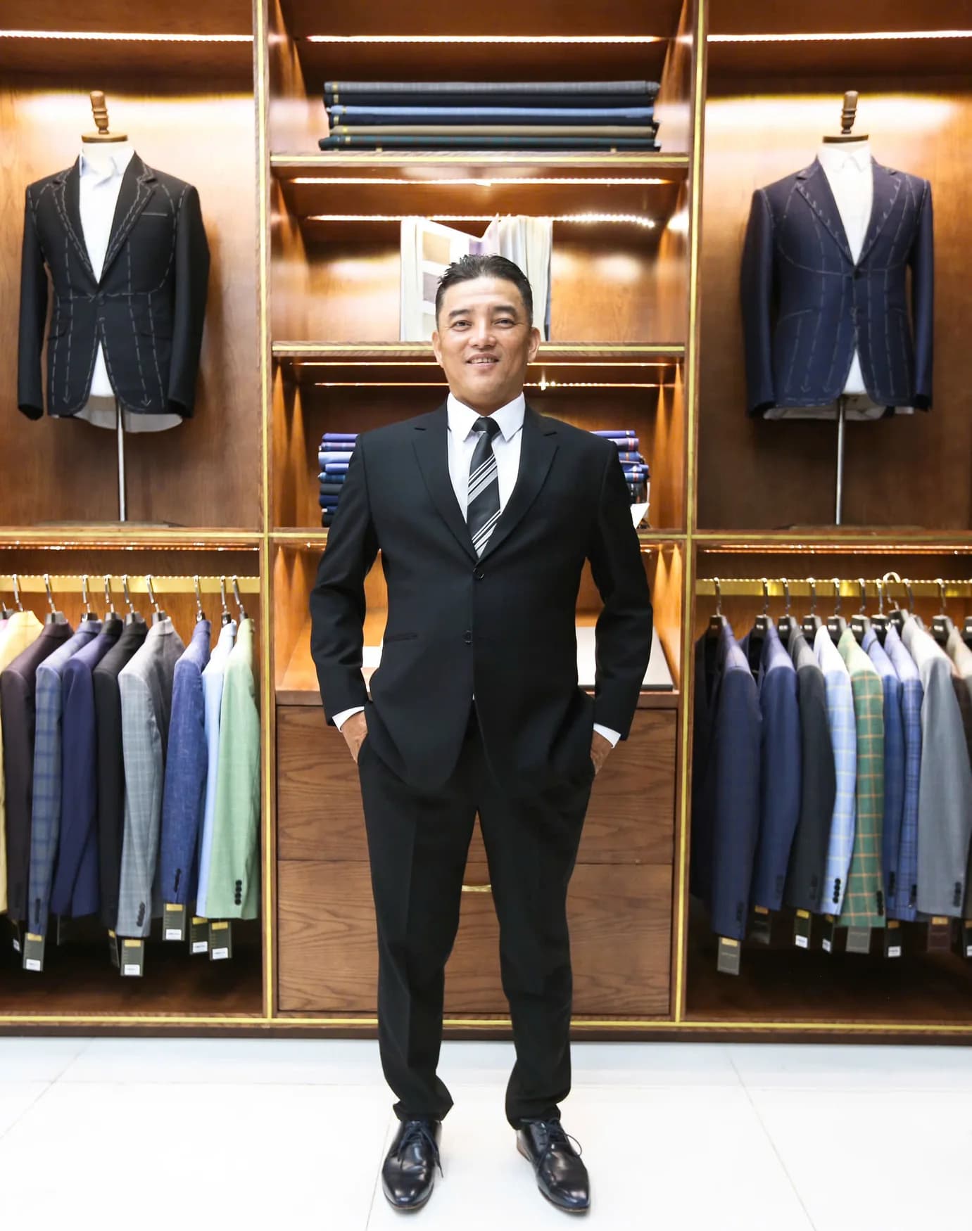 Quý ông trung niên vest đen, cà vạt sọc, trong showroom sang trọng, minh họa vest cho nam trung niên