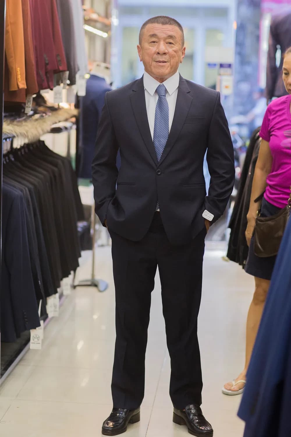 Suit navy một cúc, cà vạt xanh chấm bi, tay đút túi