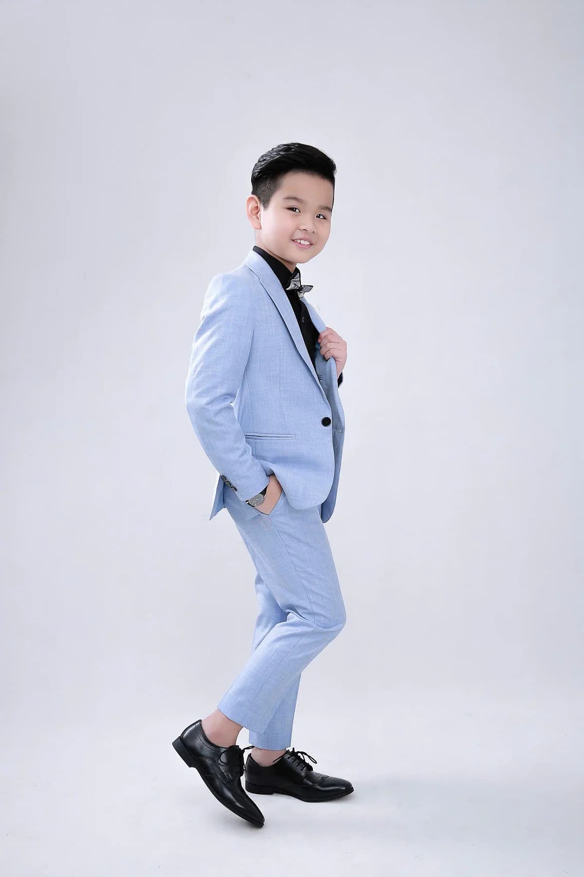 Bé trai vest xanh pastel dáng nghiêng, tay túi quần