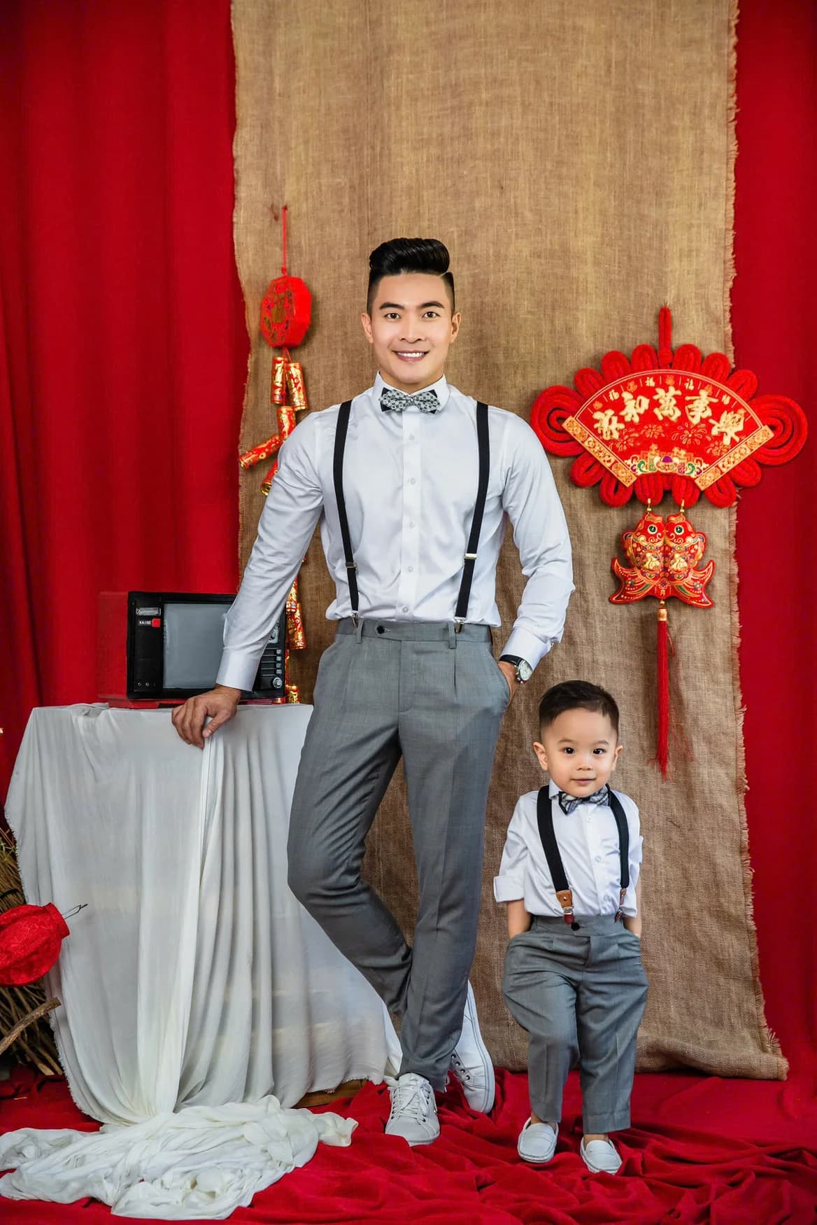 Bố và con sơ mi trắng, quần xám dây đeo, phông Tết đỏ