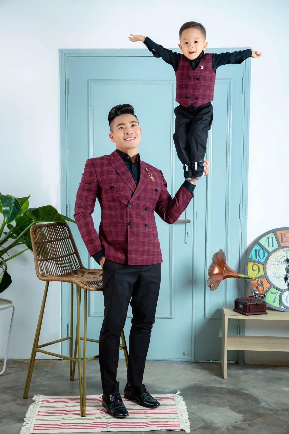 Bố nâng bé bay, vest caro đỏ mận, nền cửa xanh