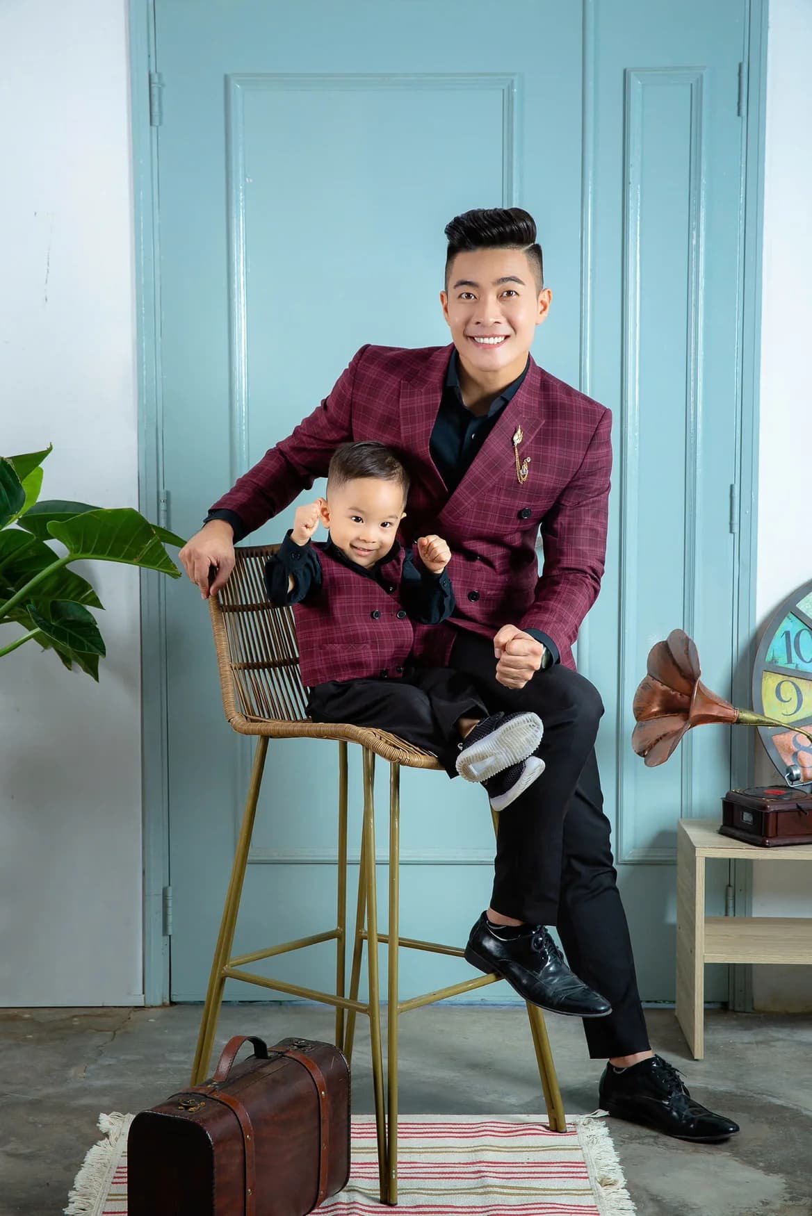 Bố con cười tươi, vest caro đỏ mận, ghế mây cao