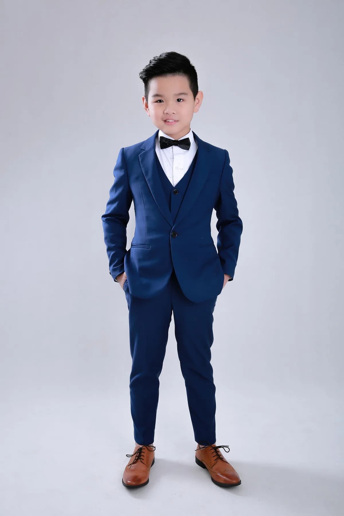 Bộ suit navy ba mảnh gọn gàng, giày da nâu, dáng đứng tự tin