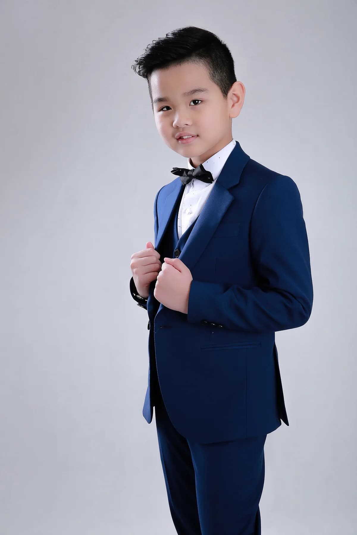 Bé nắm hai ve áo vest navy, ánh nhìn điềm tĩnh và cuốn hút