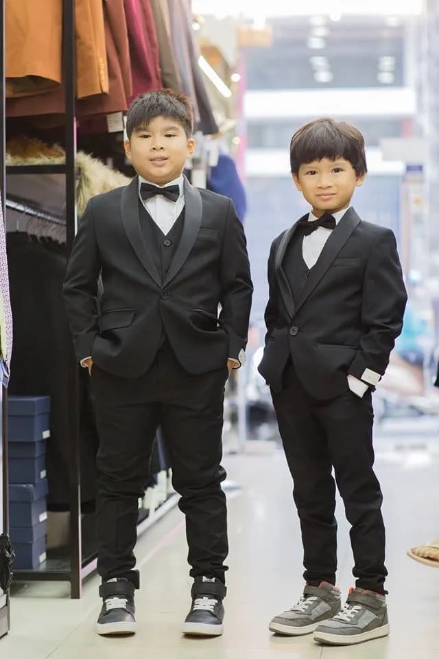 Hai cậu bé diện tuxedo đen, nơ đen đứng cạnh nhau trong cửa hàng