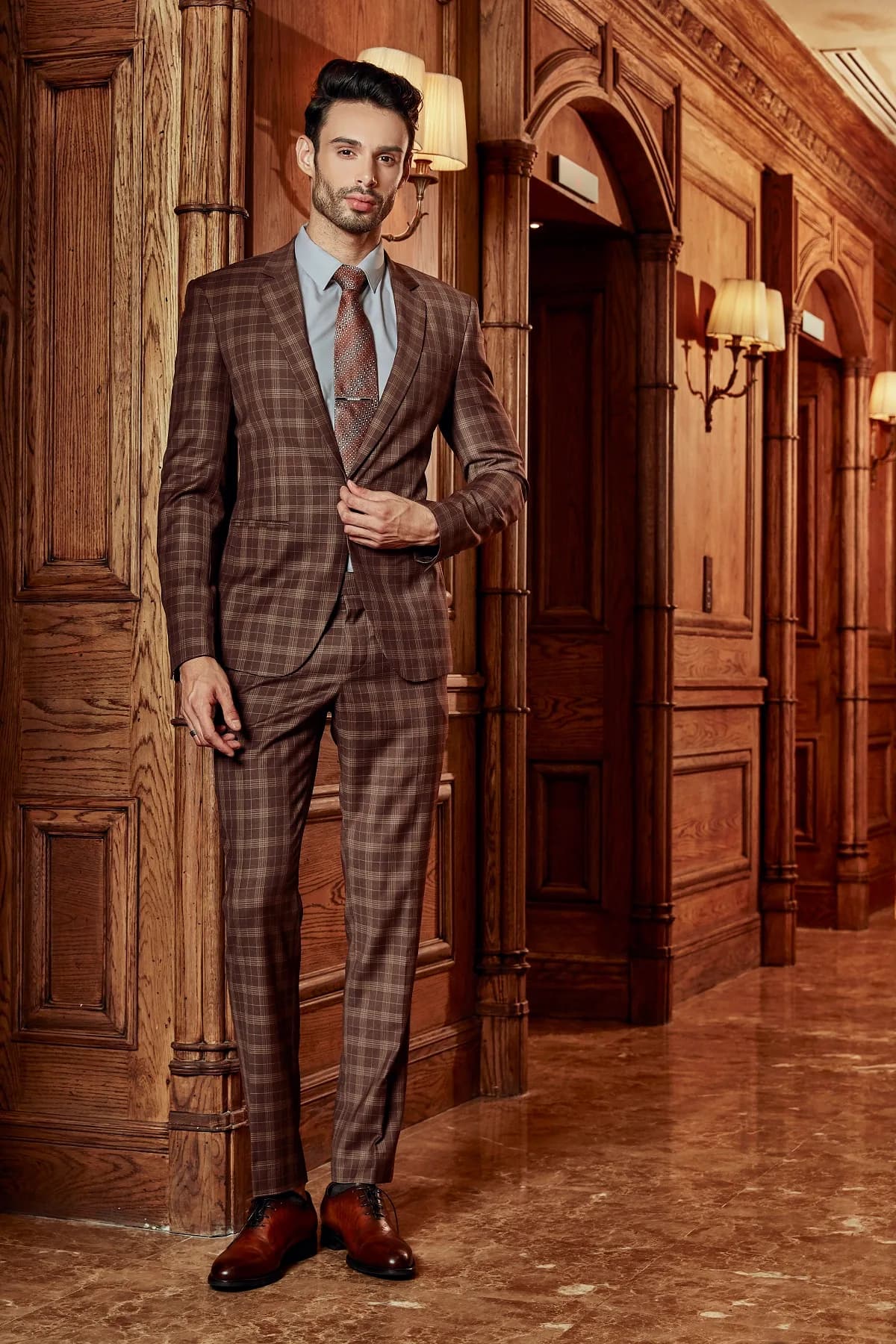 Suit caro nâu chocolate phối sơ mi xanh nhạt, kẹp cà vạt, đứng hành lang gỗ