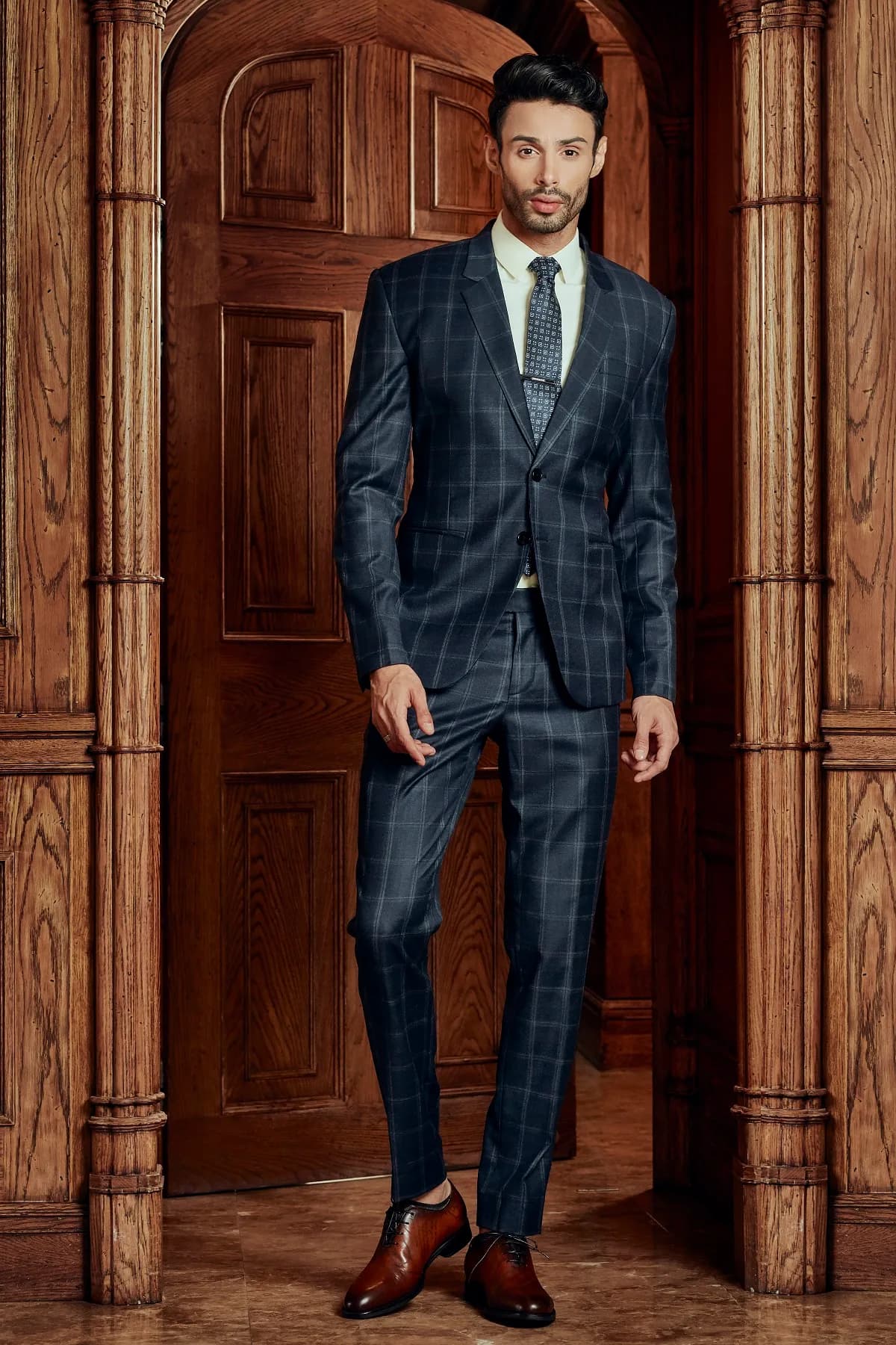 Suit kẻ ô xanh navy, cà vạt họa tiết, đứng giữa khung cửa vòm gỗ