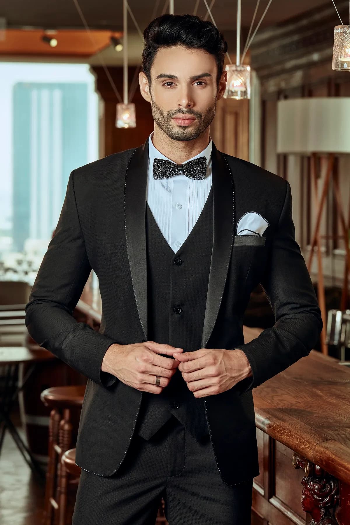 Tuxedo đen ba mảnh ve satin, nơ họa tiết, khăn cài túi xanh nhạt, bên quầy bar