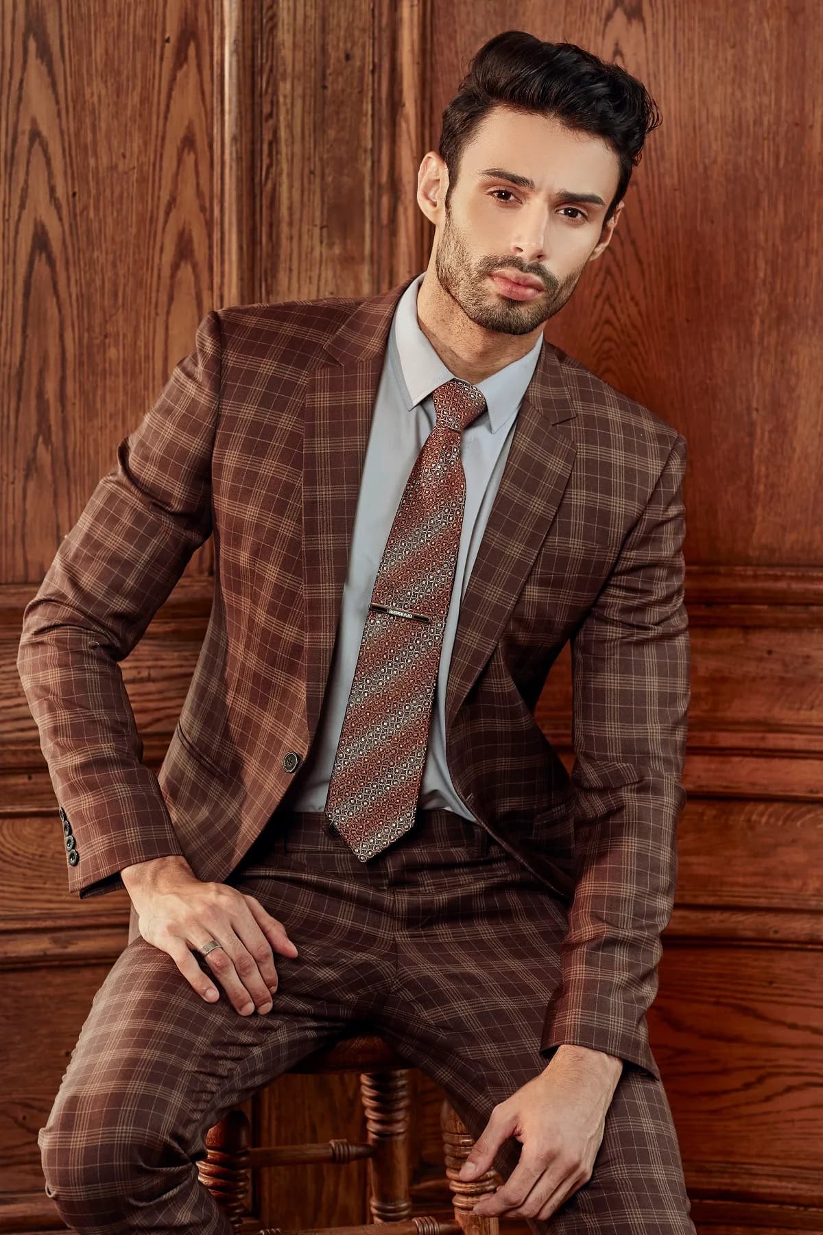 Suit kẻ ô nâu đỏ, cà vạt cùng tông, ngồi ghế cao nhìn thẳng