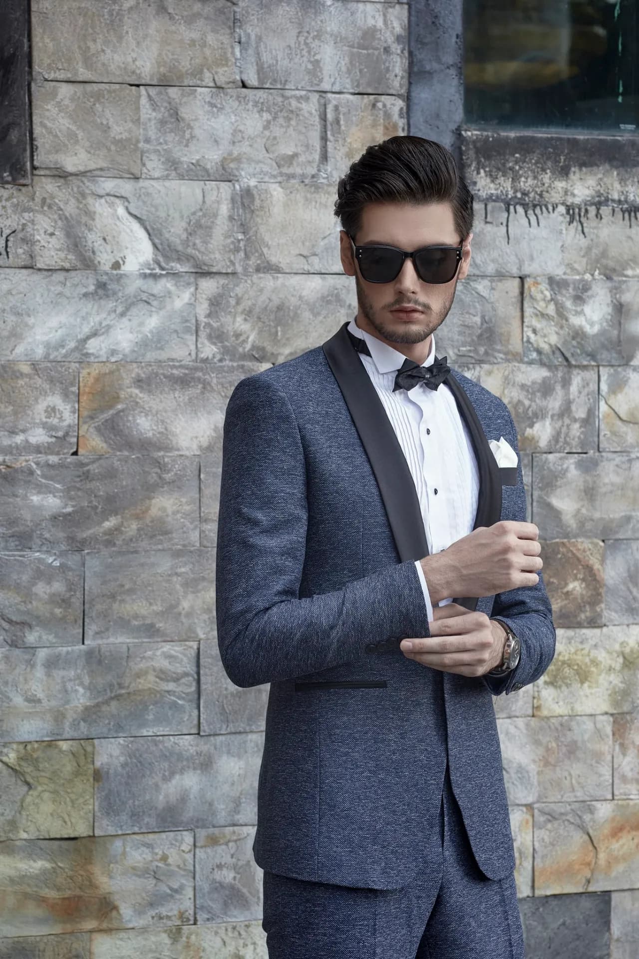 Tuxedo xanh navy ve nhung đen, kính râm, chỉnh khuy măng sét, tường đá