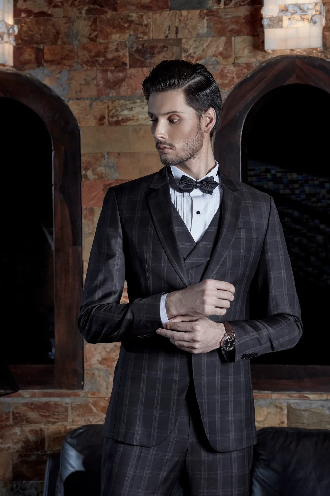 Suit ba mảnh kẻ ô tối màu, nơ đen, chỉnh khuy măng sét, nền vòm gạch