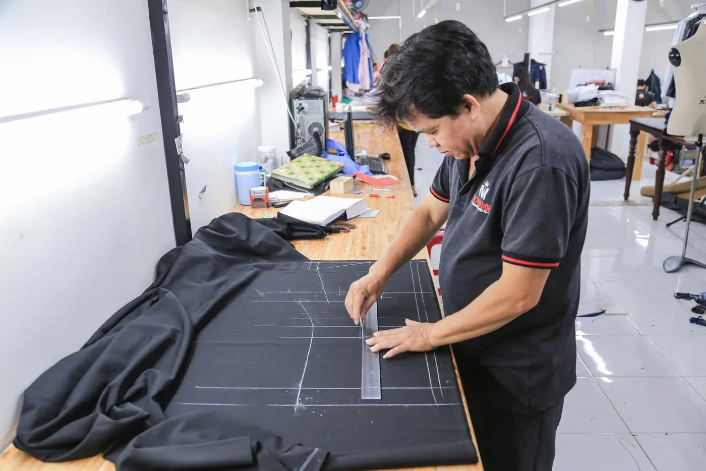 Nghệ nhân nam áo polo đen viền đỏ kẻ rập trên vải đen, bước đầu của quy trình may đo vest nam